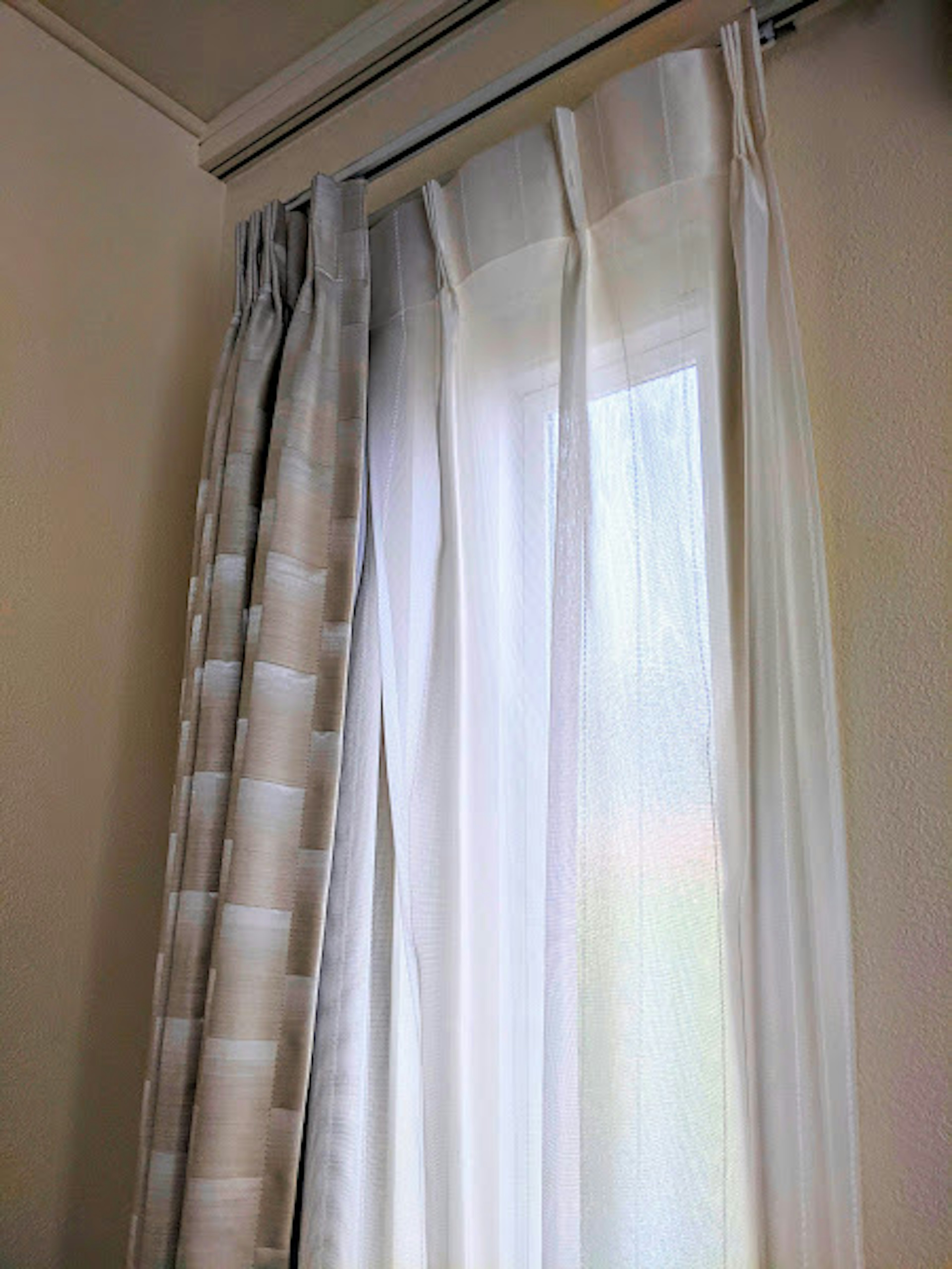 Sheer white curtains and patterned drapes frame a window