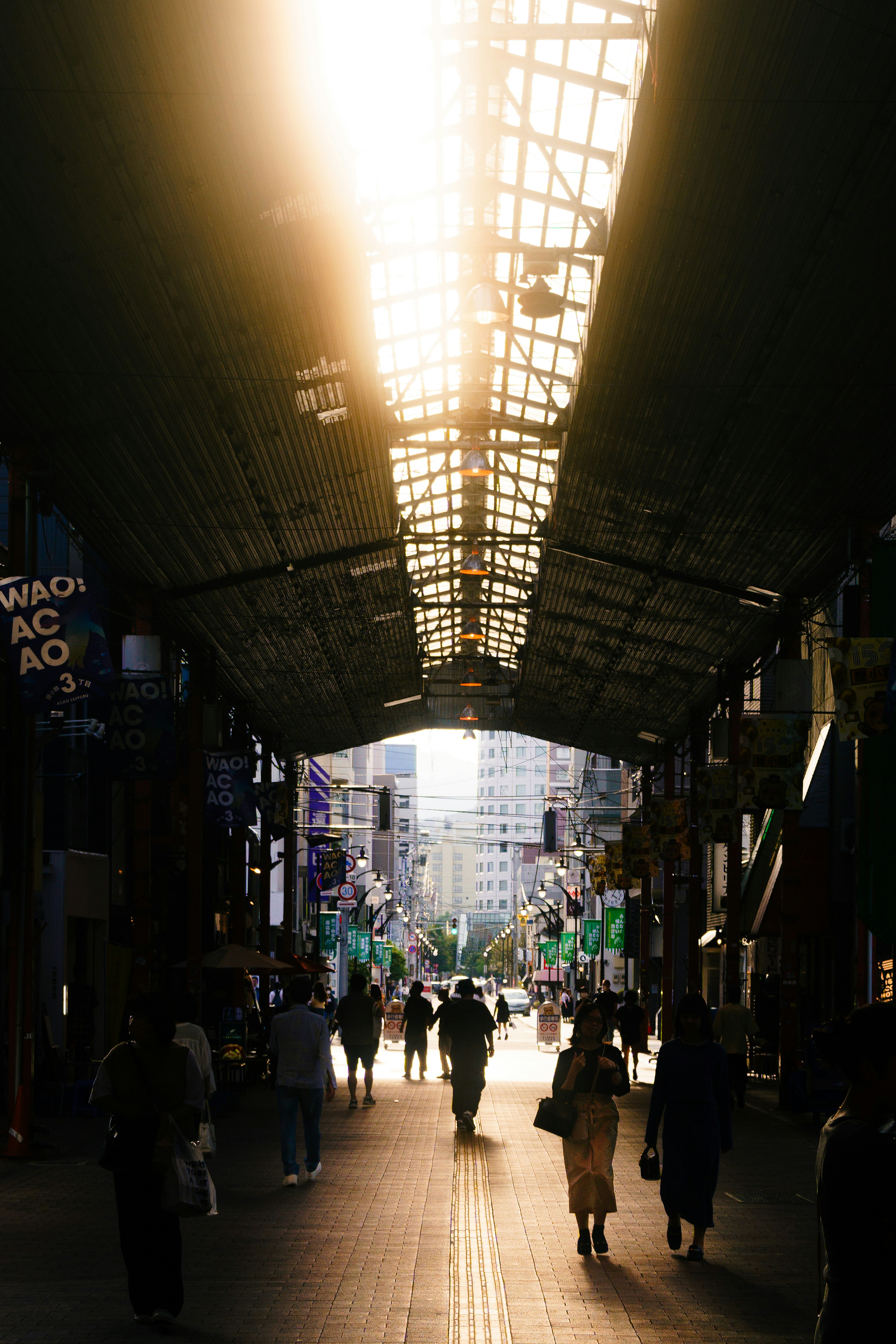 Silhouette de personas caminando en una calle comercial con luz brillante que entra por el techo