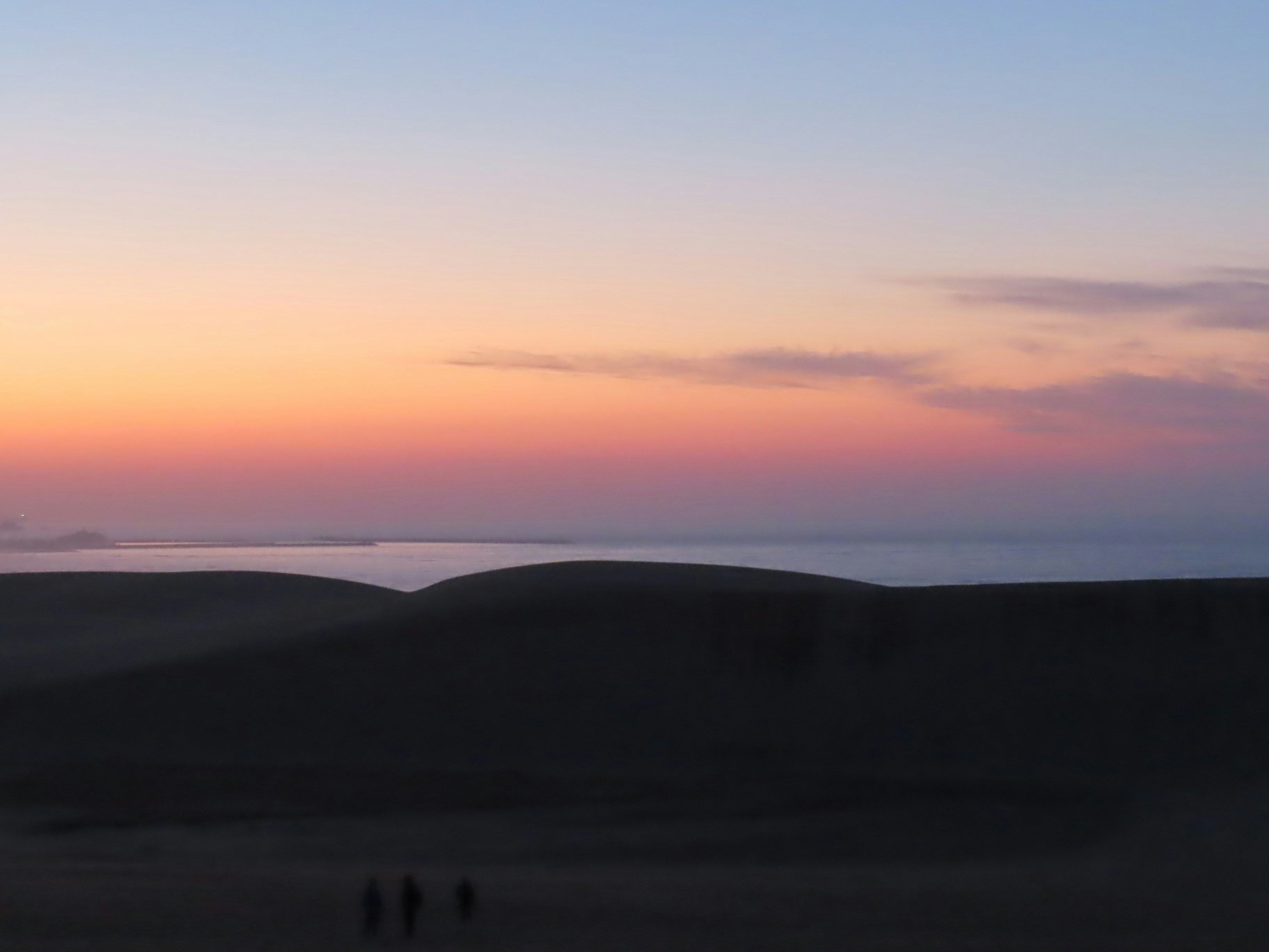 Sunset over the ocean with silhouettes of people on sand dunes