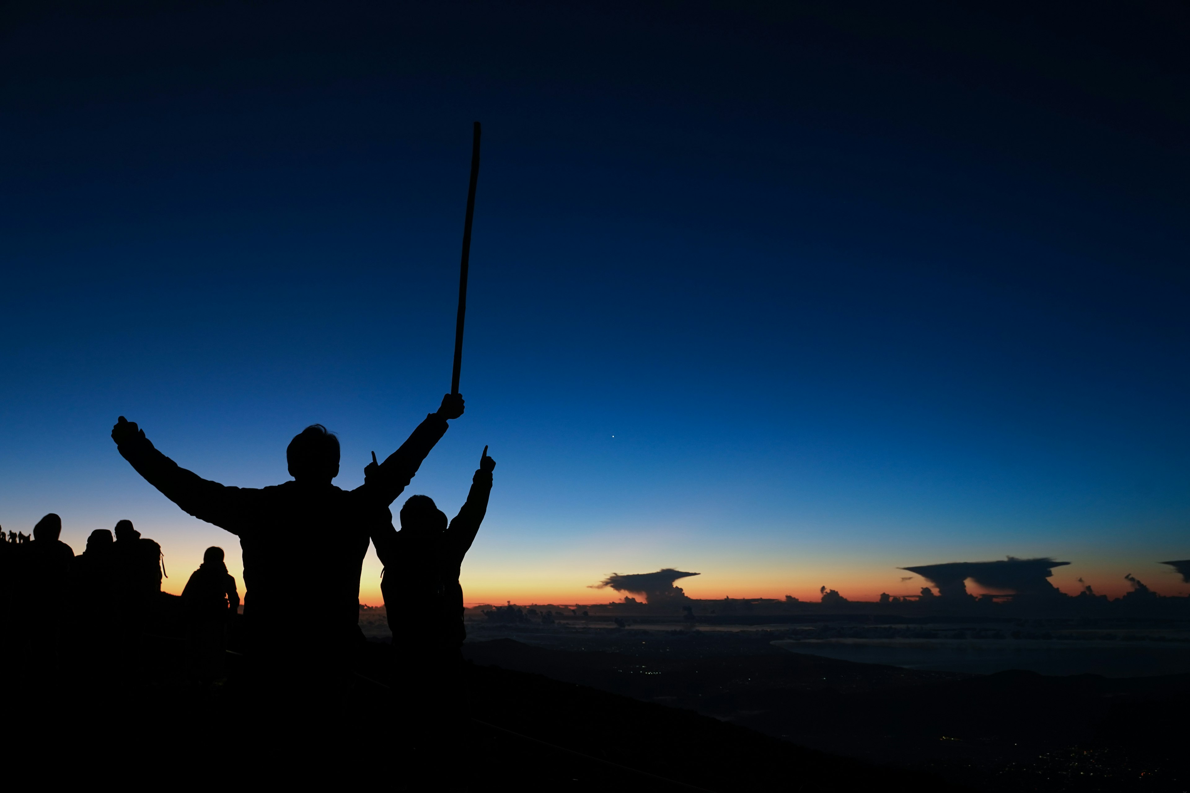 Silhouetten von Personen, die ihre Arme im Sonnenuntergang heben, mit einem Farbverlauf am Himmel