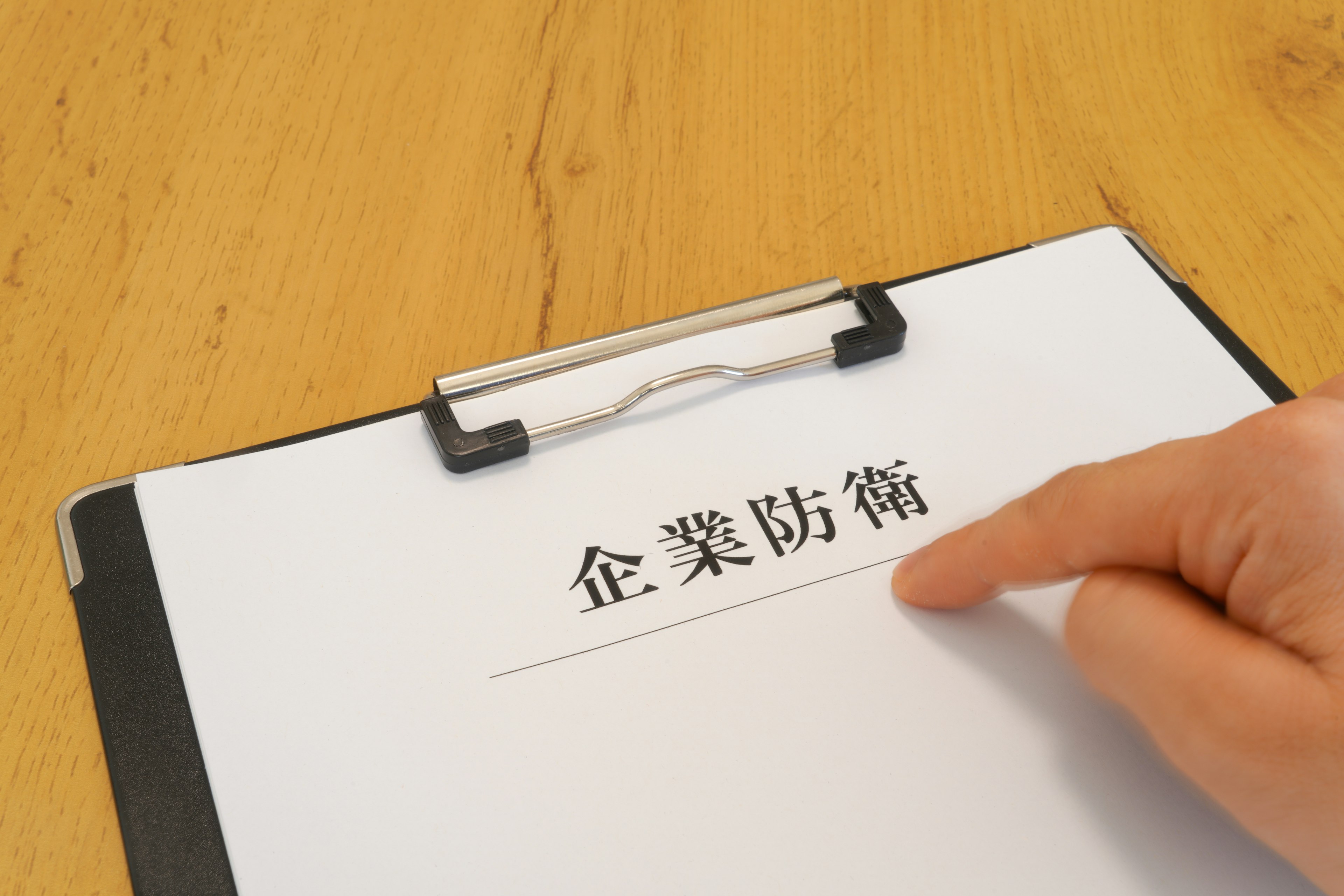 A hand pointing at a document titled 'Corporate Defense' on a clipboard on a wooden surface