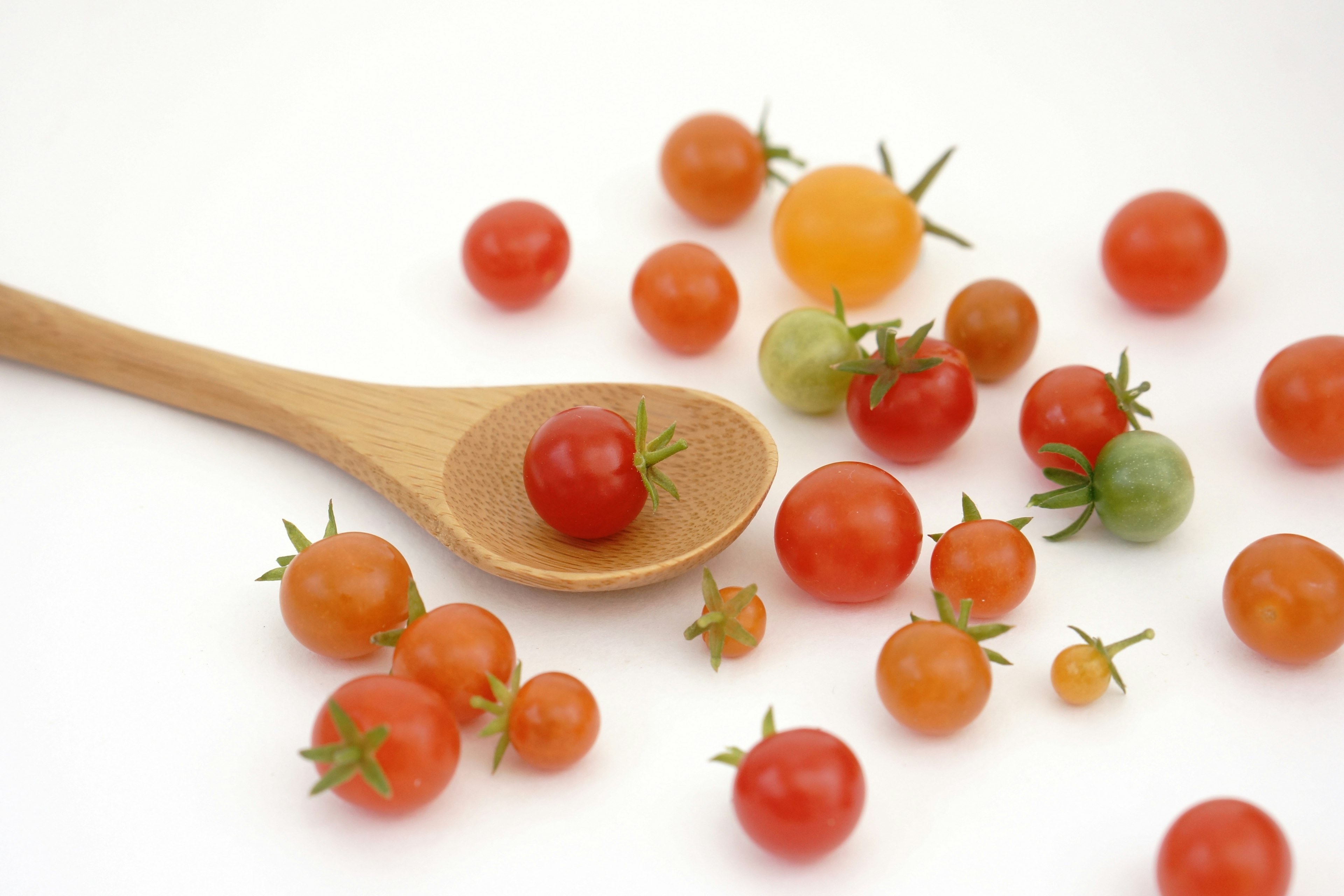 Various sizes of cherry tomatoes scattered around a wooden spoon with one tomato resting on it