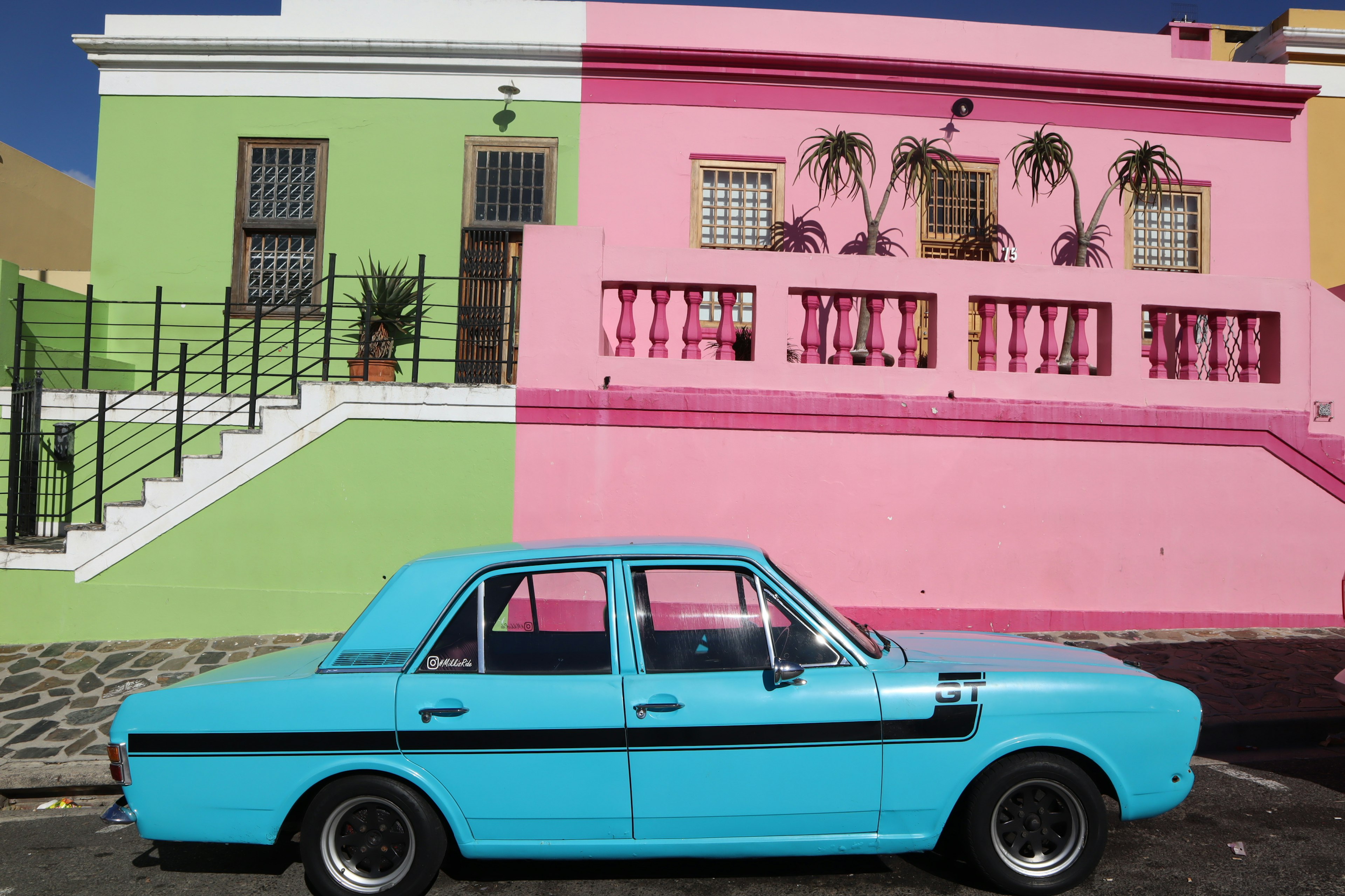 A bright blue car parked in front of colorful pink and green buildings