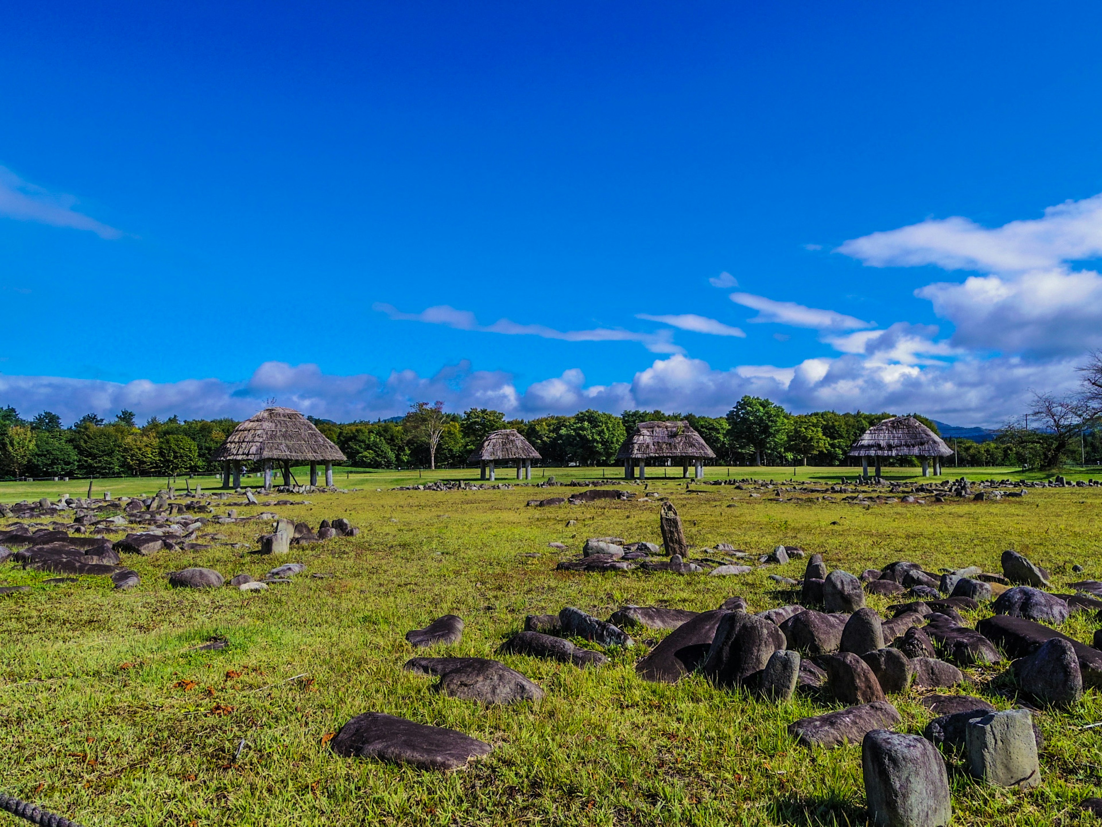 Pemandangan dengan lapangan rumput dan reruntuhan batu kuno di bawah langit biru