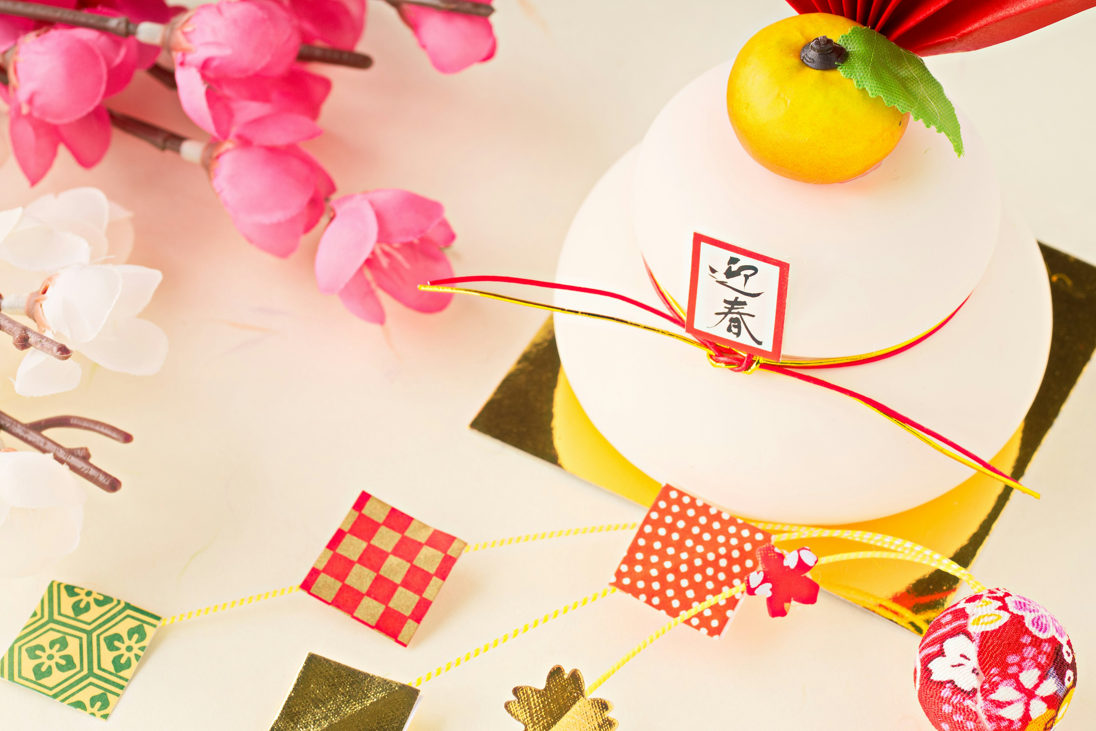 Decorative rice cake topped with a mandarin orange and tied with a red ribbon surrounded by cherry blossoms