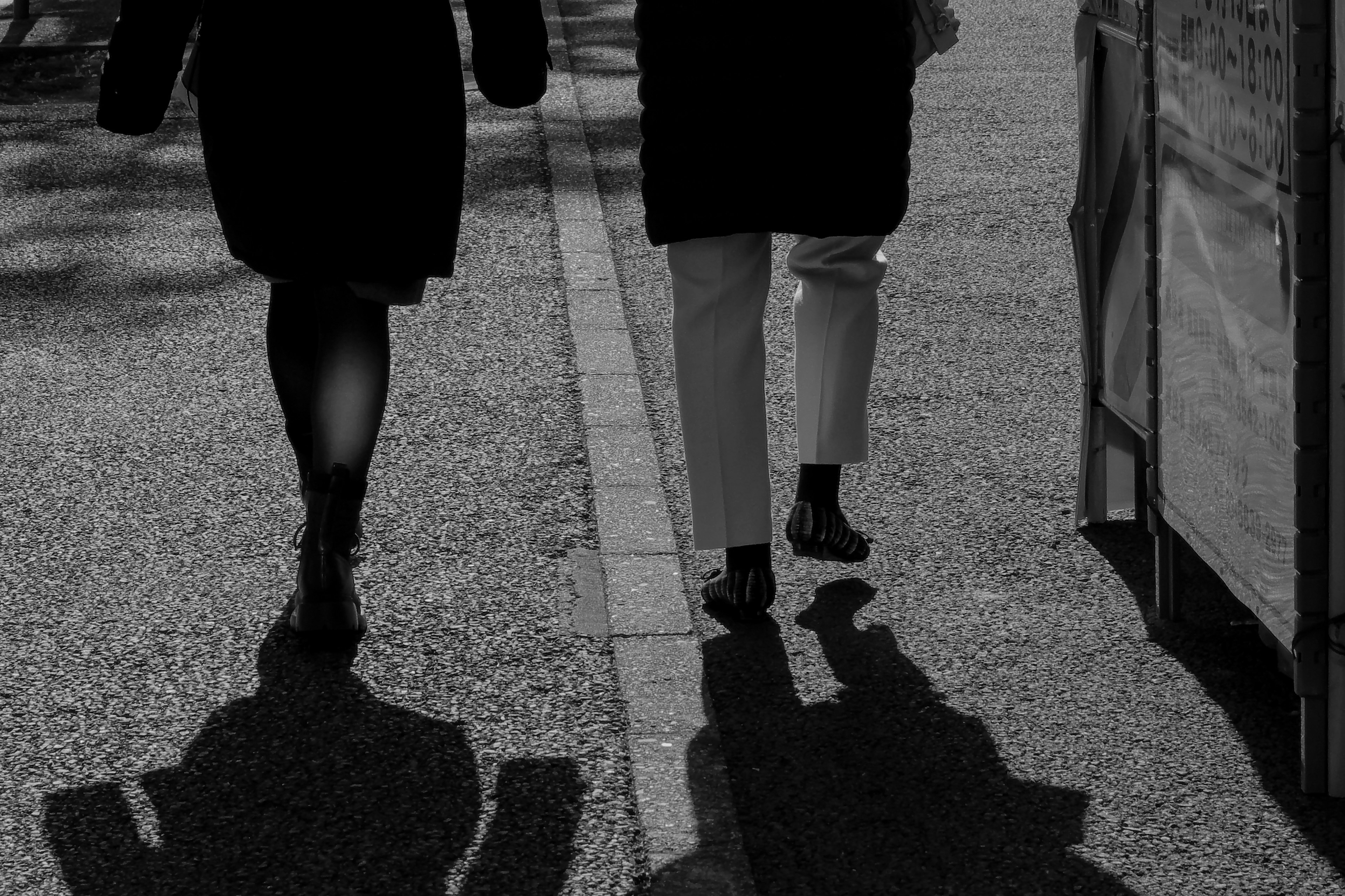 Dos figuras caminando con sombras en una calle en blanco y negro