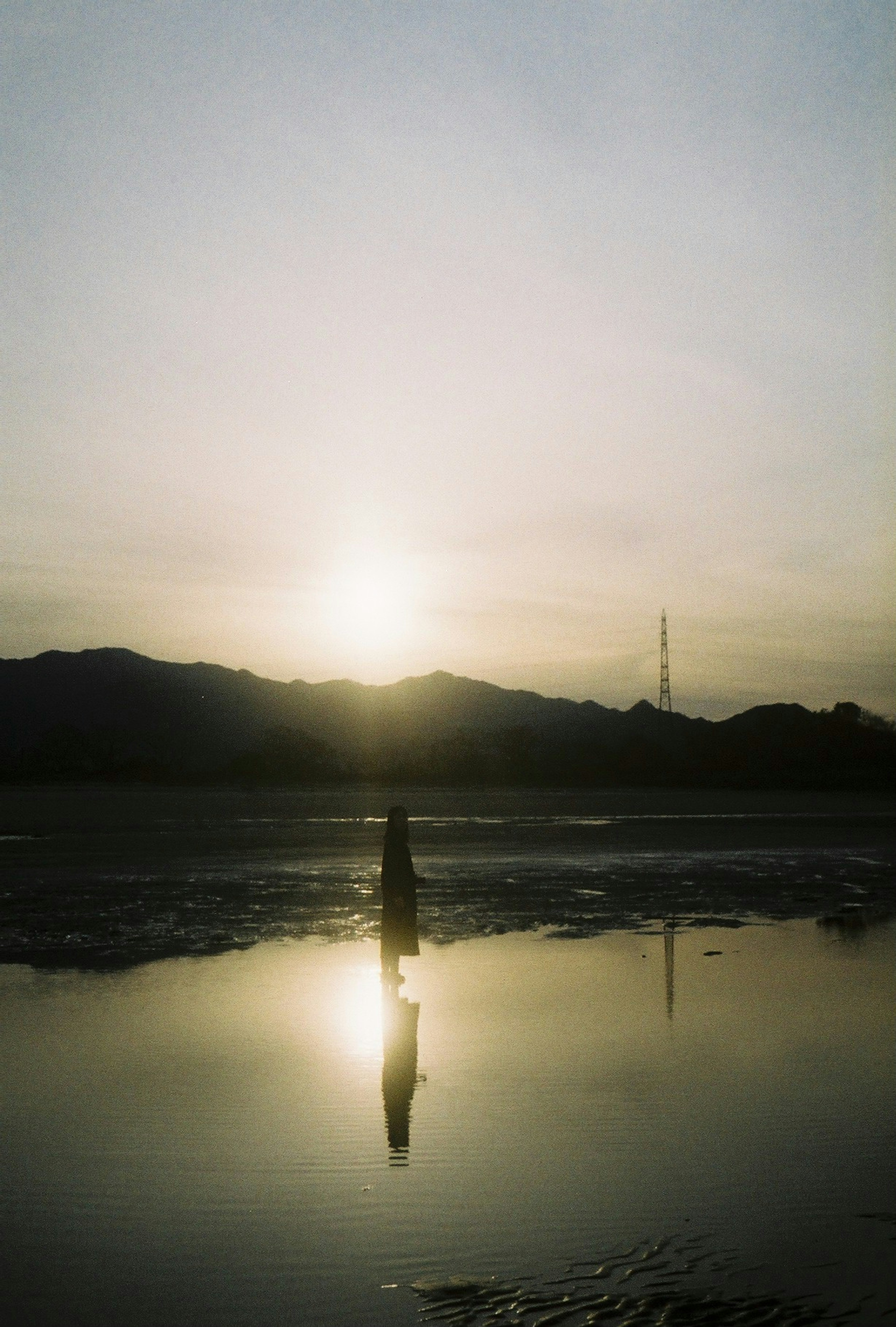 Silhouette of a person reflected in water at sunset with mountains in the background