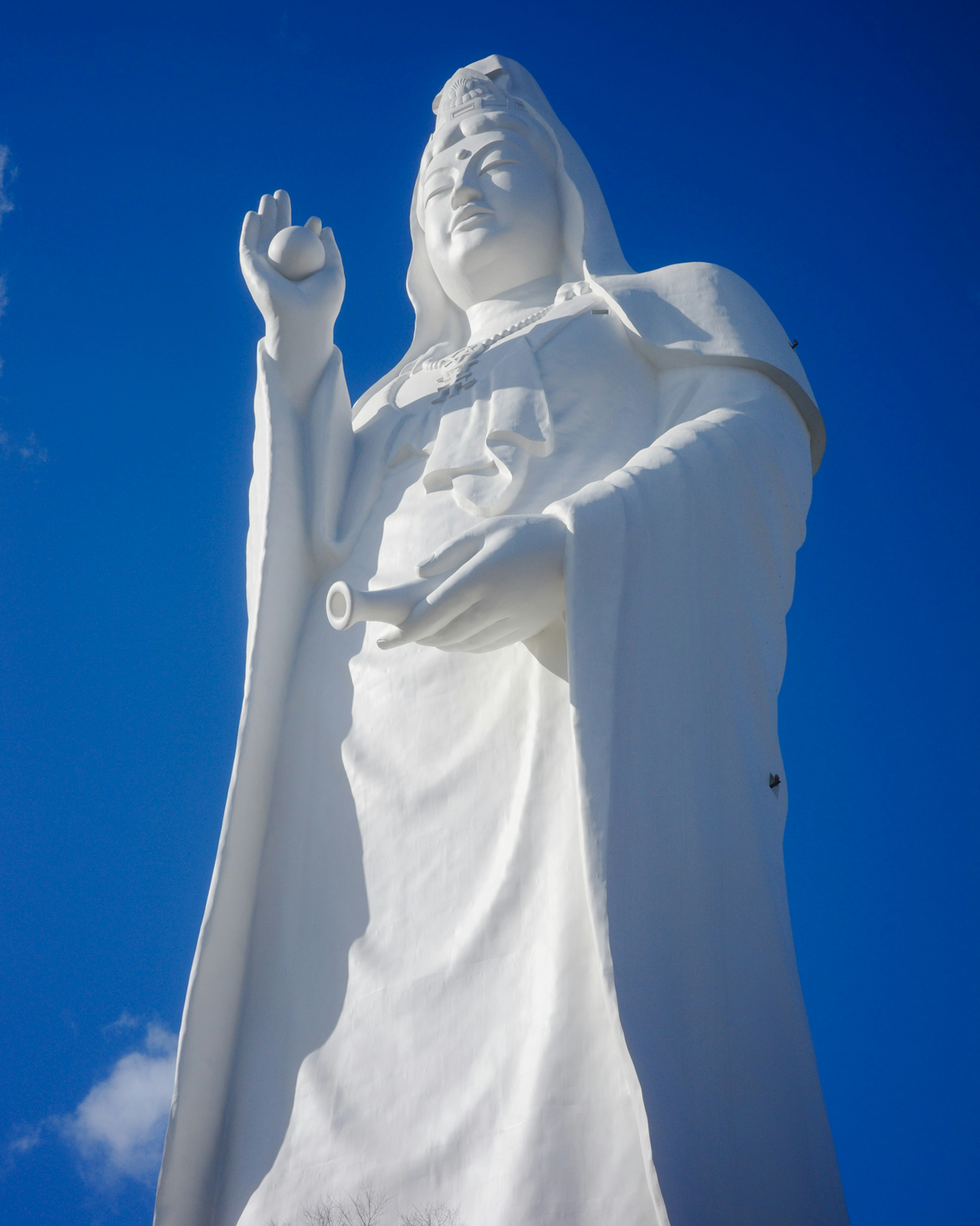 Une statue blanche de Guanyin se tenant sous un ciel bleu