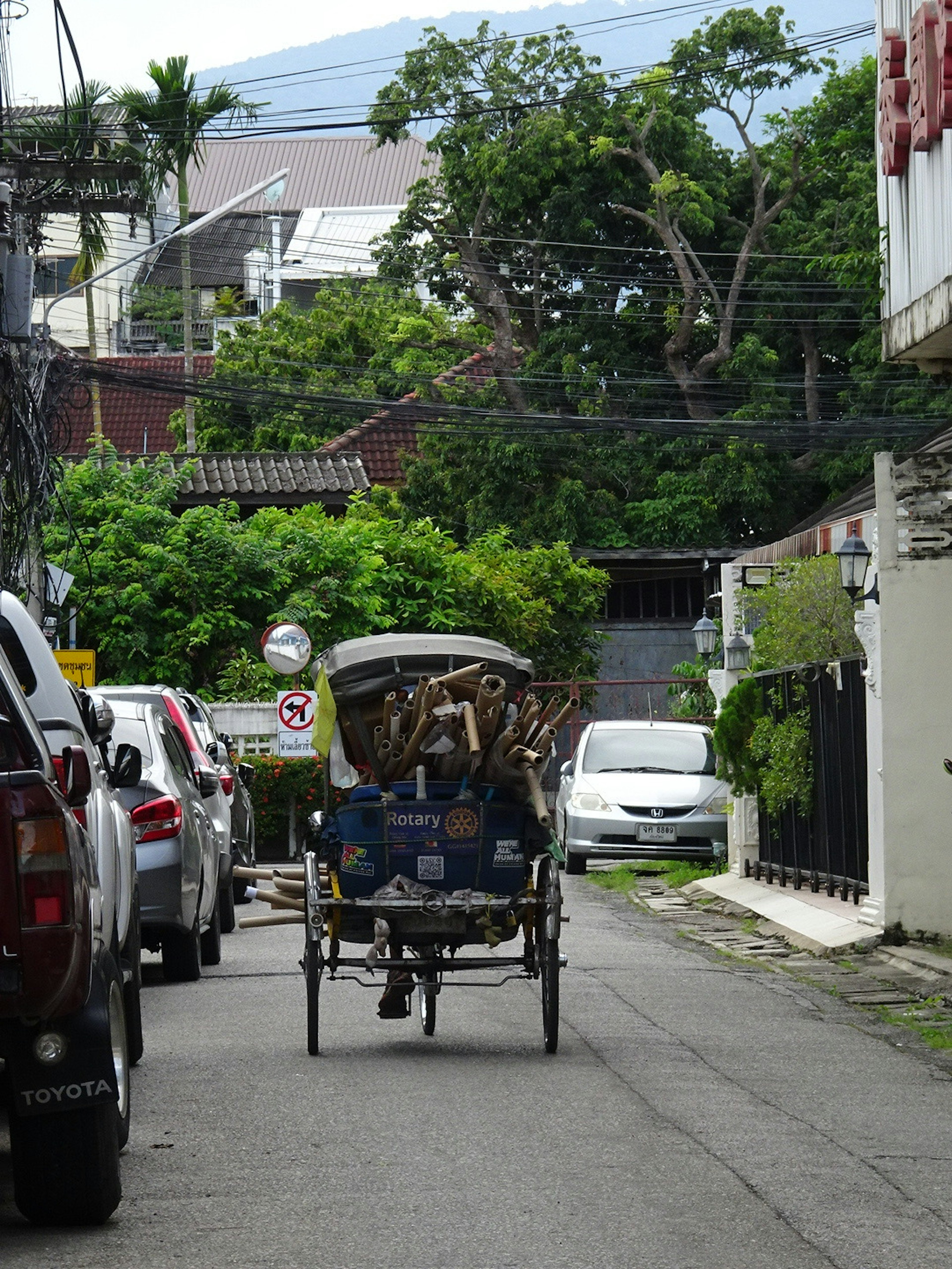 A tricycle taxi on a narrow street surrounded by parked cars and greenery