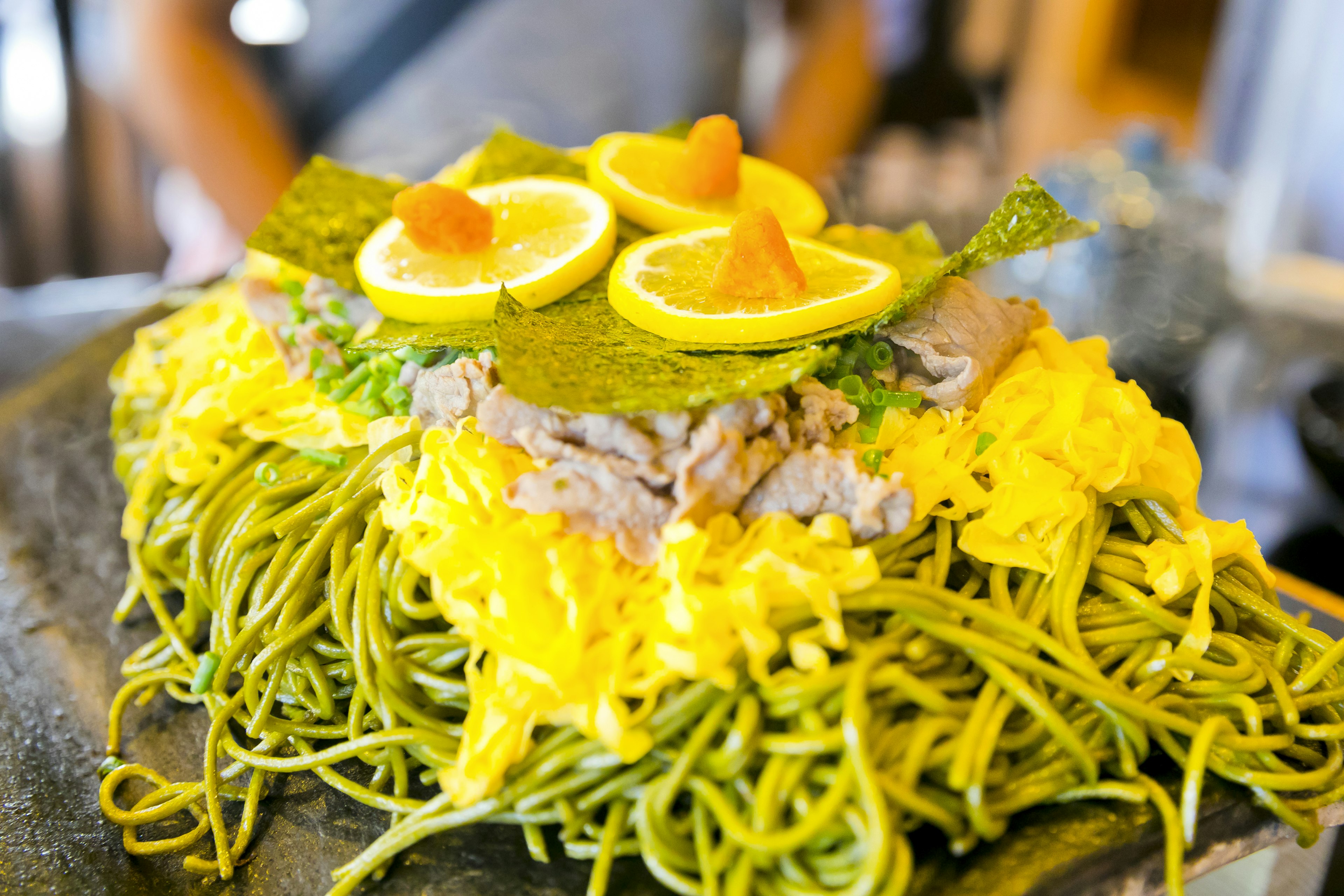 Plato con fideos verdes cubiertos con huevo amarillo y rodajas de limón