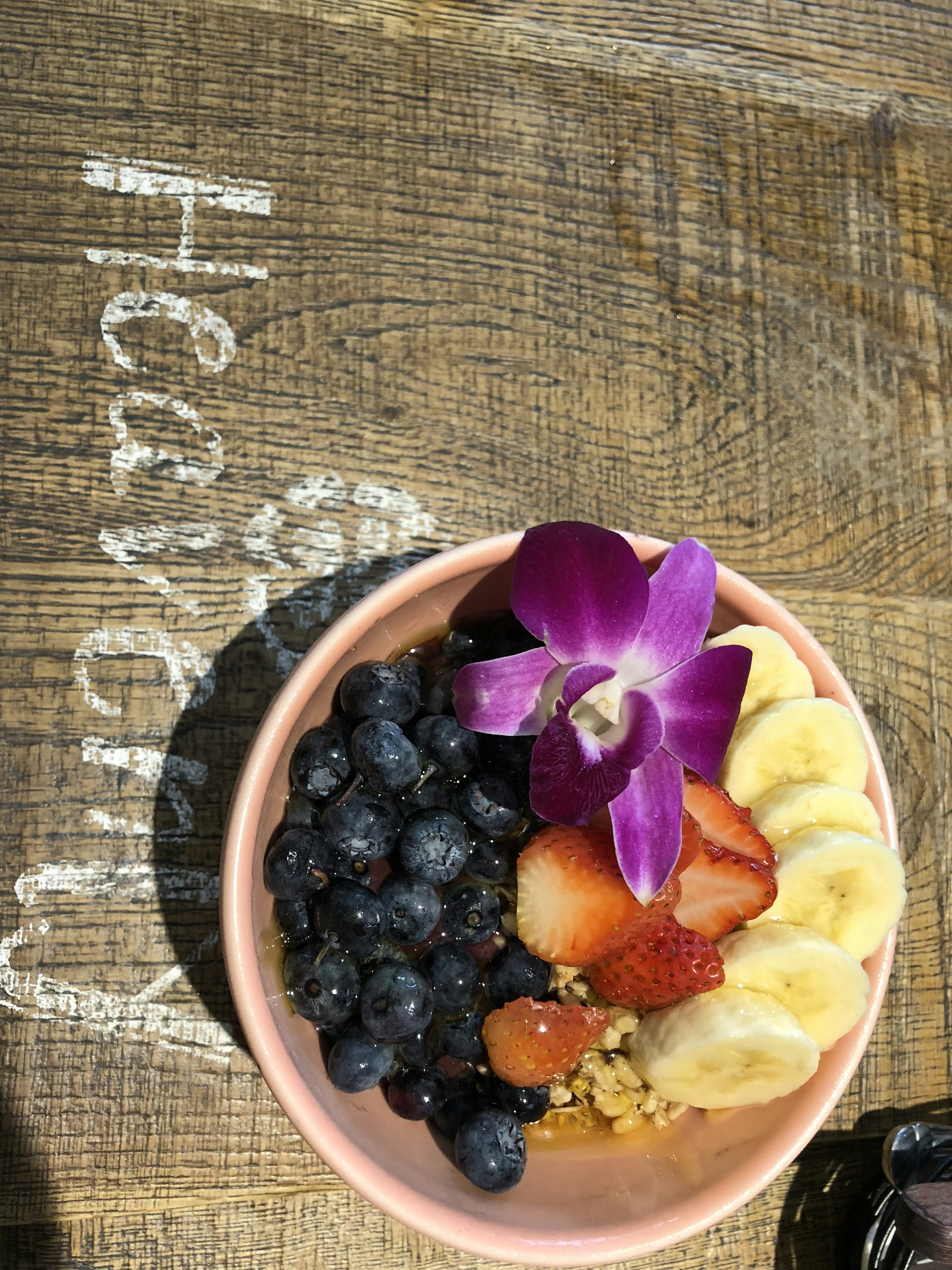 Una ciotola piena di frutta colorata tra cui mirtilli banane e fragole guarnita con un fiore viola