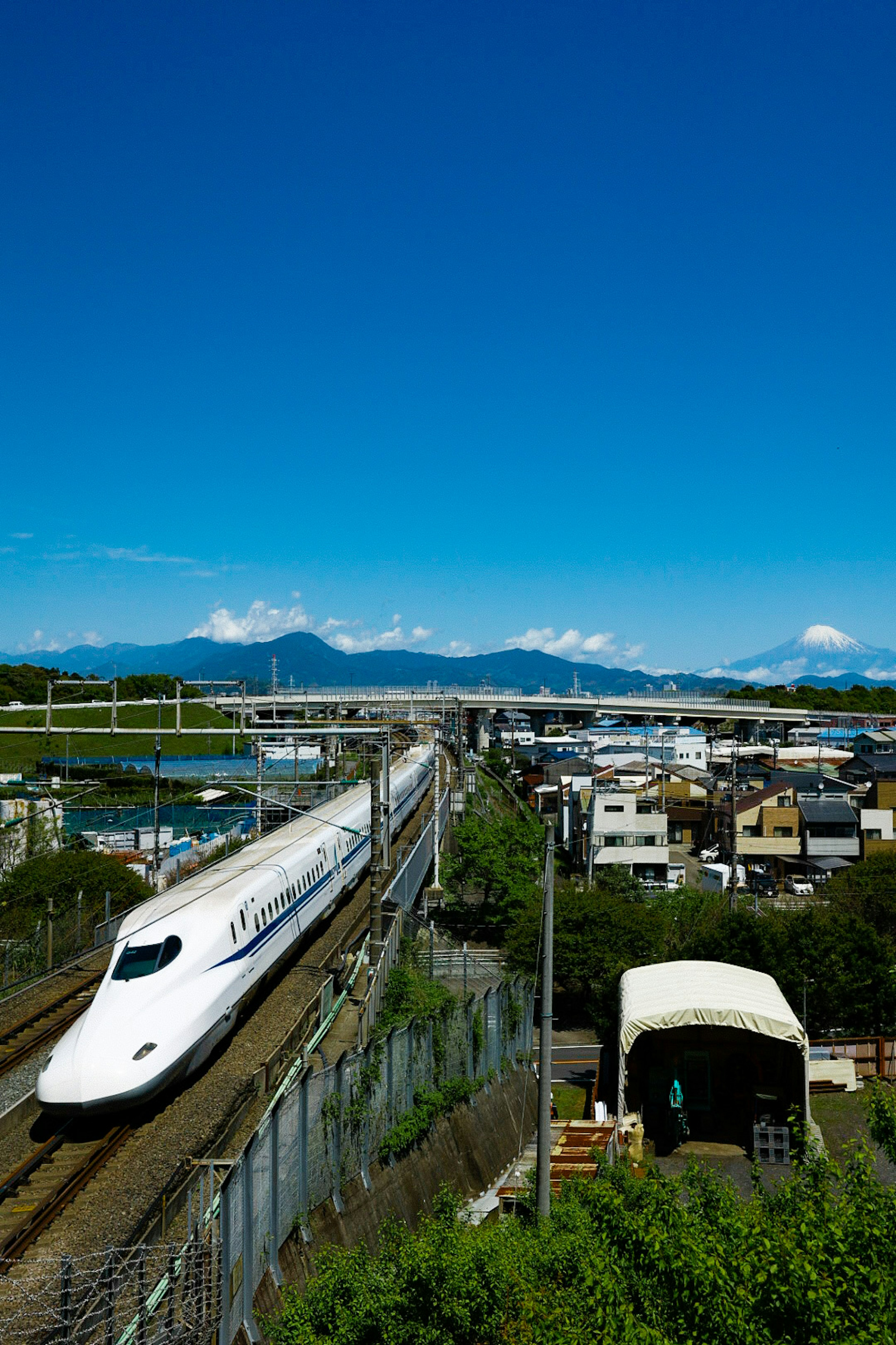 Shinkansen traveling under a clear blue sky with mountains and city in the background