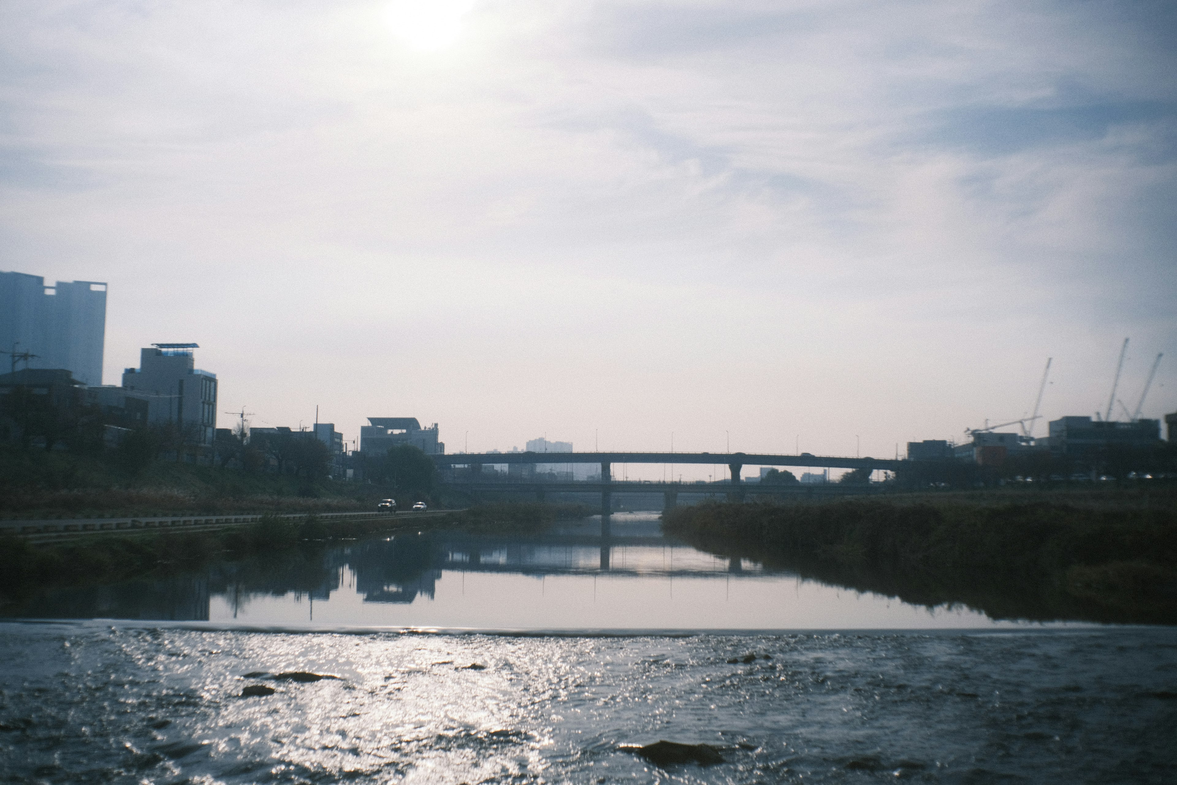 Urban landscape featuring a river and bridge under soft evening light