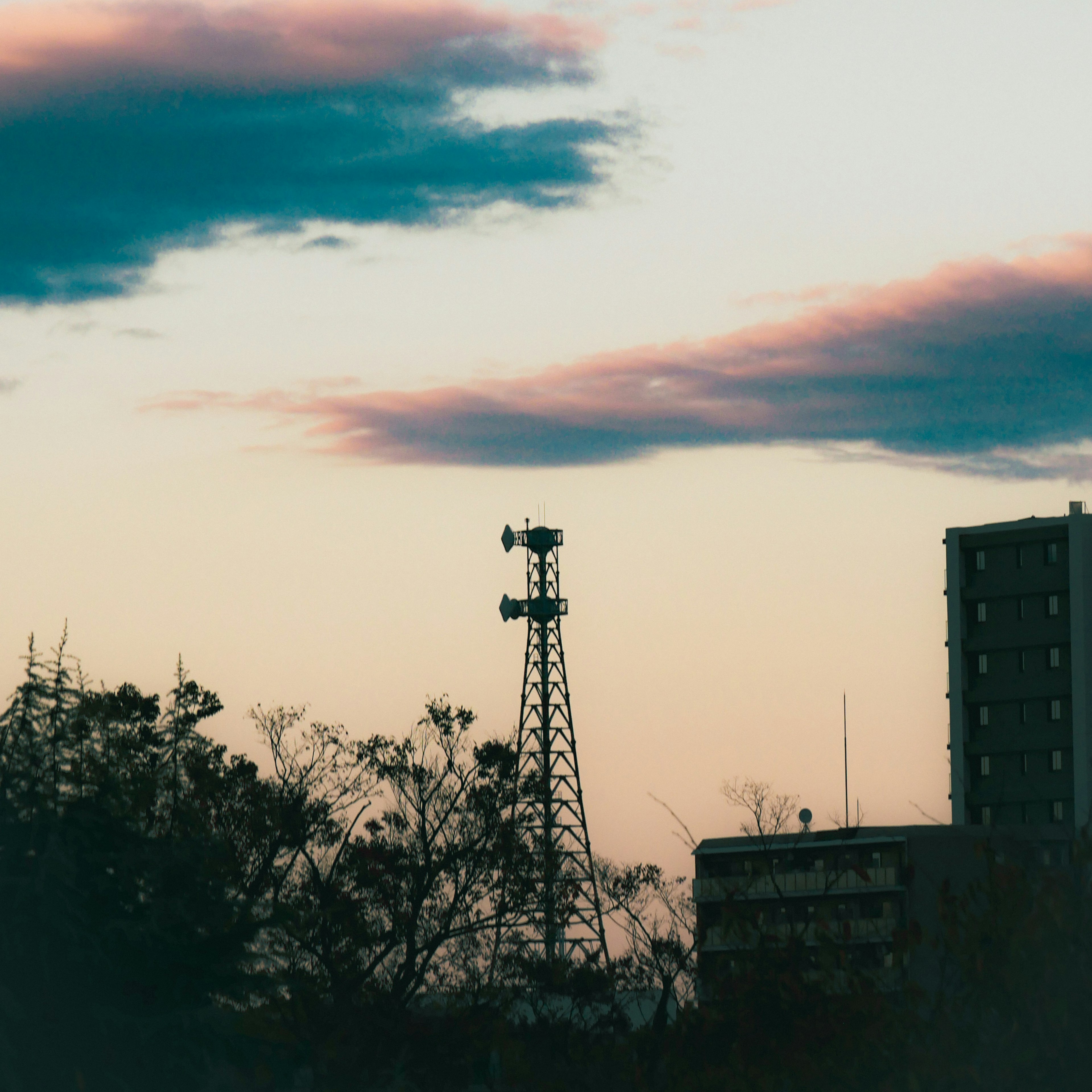 Silhouette of a communication tower and building against a dusk sky