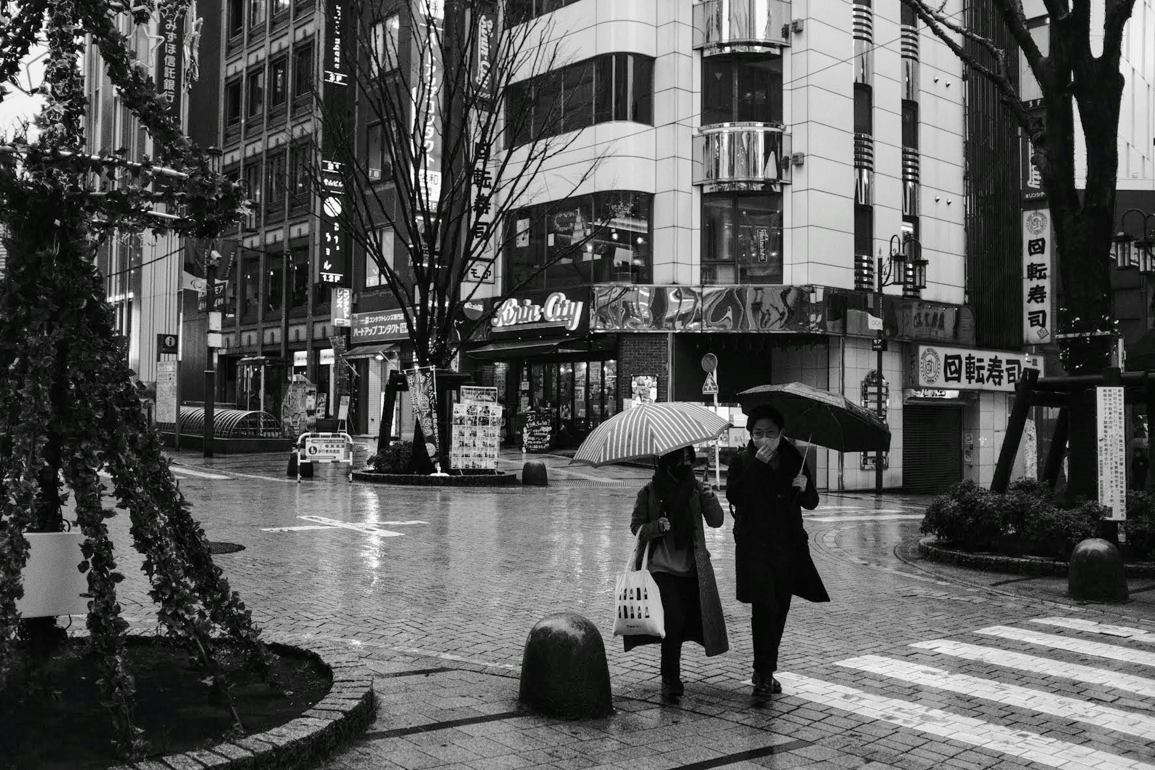 雨の中で傘をさして歩く二人の人物と街の景観