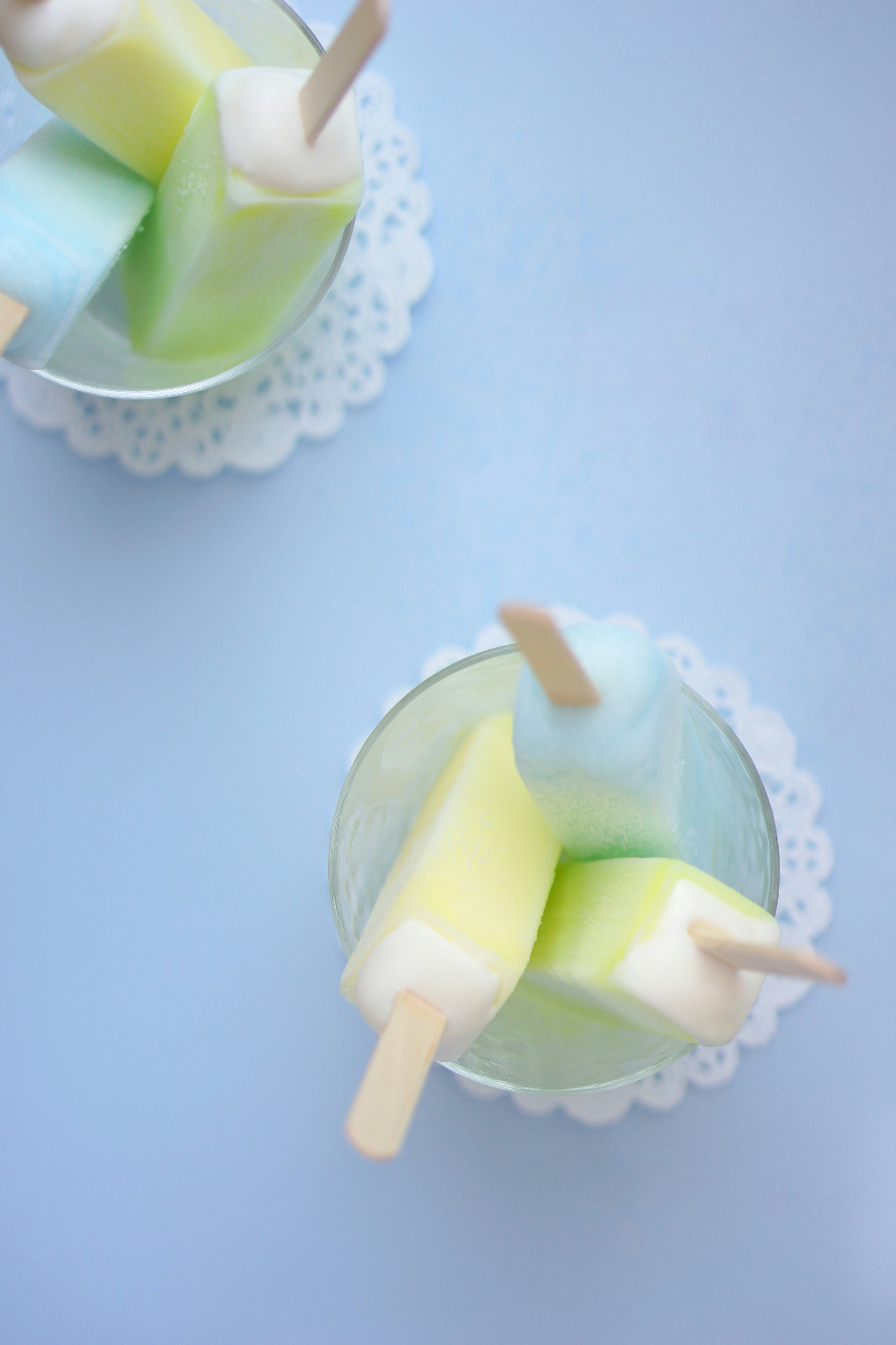 Des popsicles colorés dans un plat en verre sur un fond bleu clair