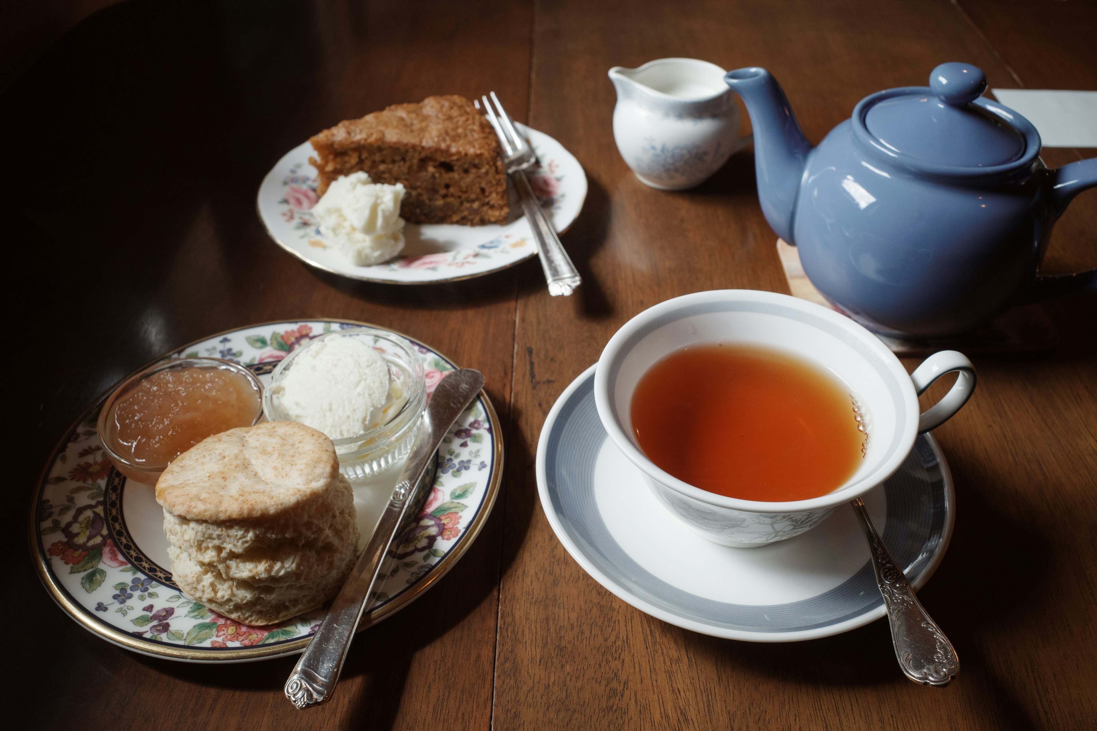 Sebuah meja dengan teko dan cangkir teh serta scone dan kue di piring bermotif bunga