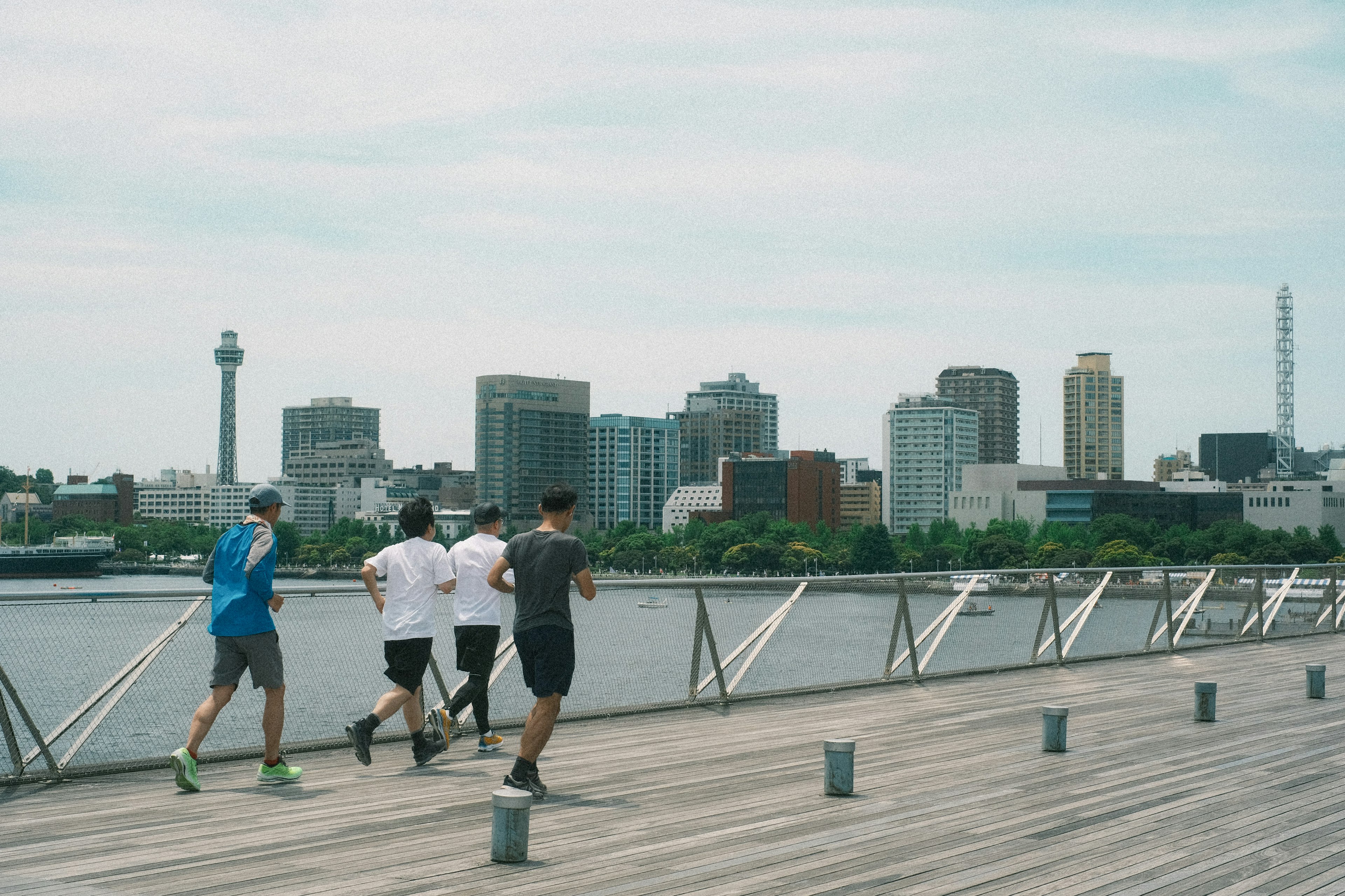 Vier Männer joggen auf einem Holzsteg mit einer Stadtsilhouette im Hintergrund