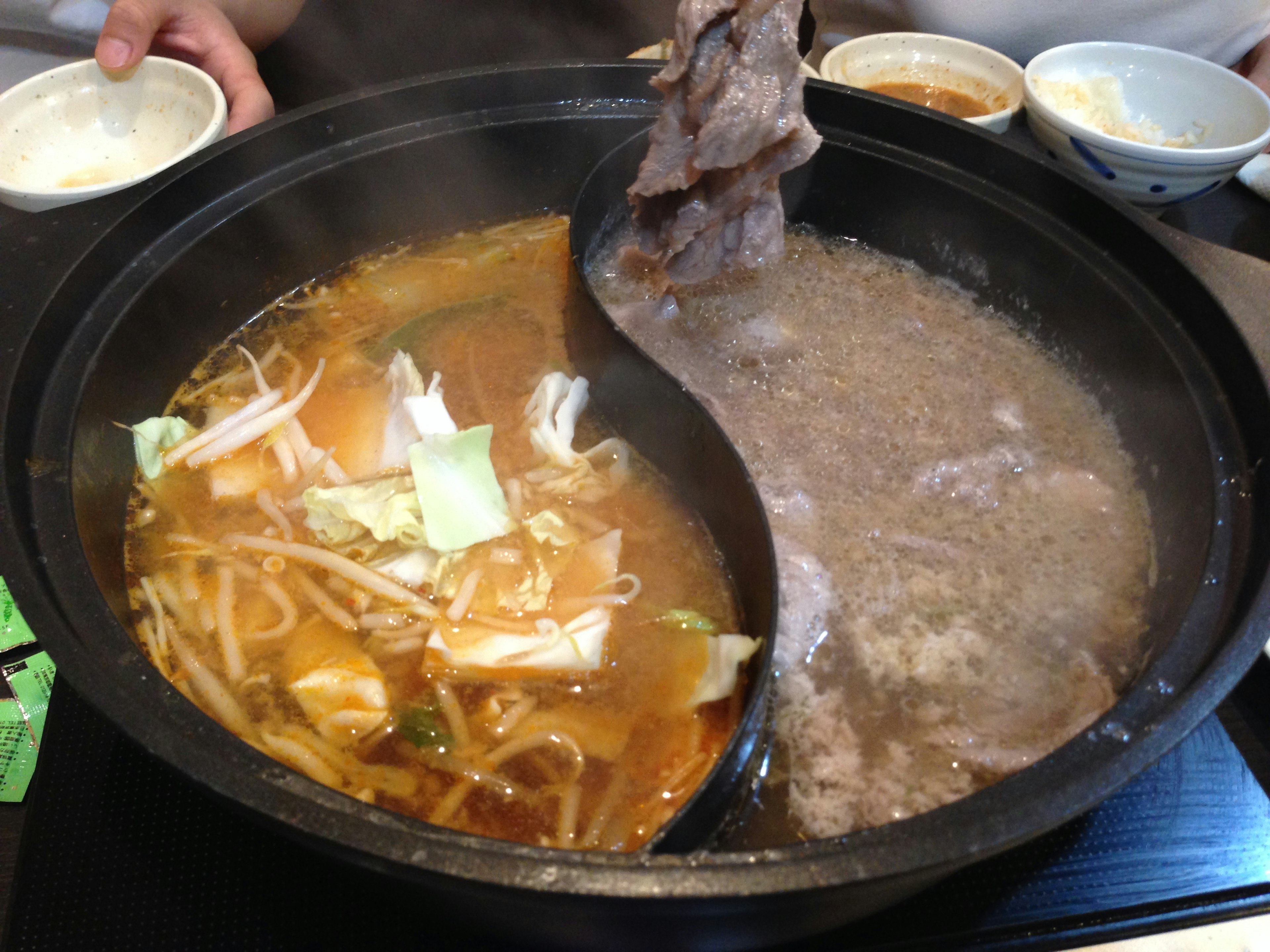 A hot pot with two divided soup sections featuring fresh vegetables and meat