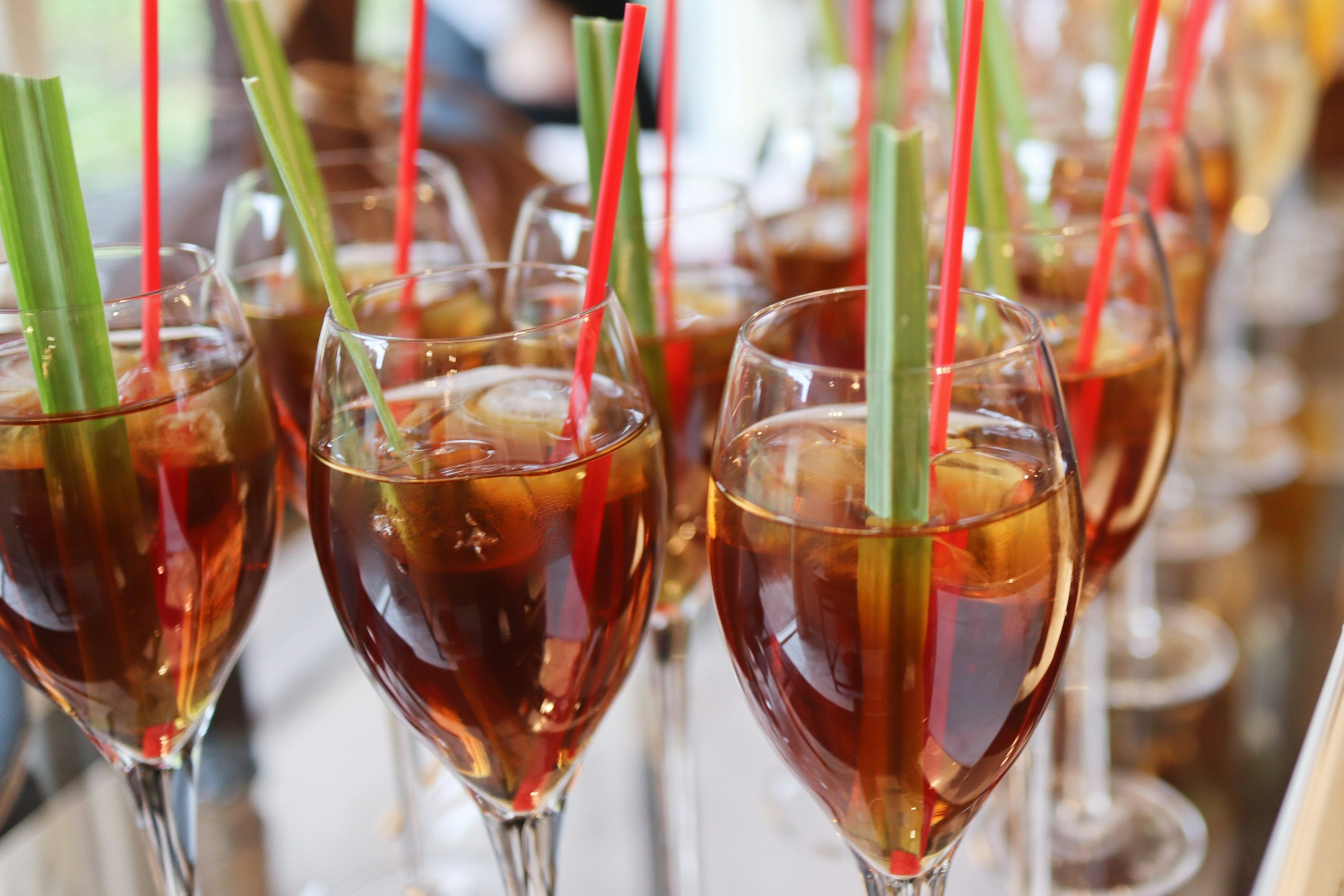 A row of cocktail glasses filled with colorful drinks featuring straws and celery sticks