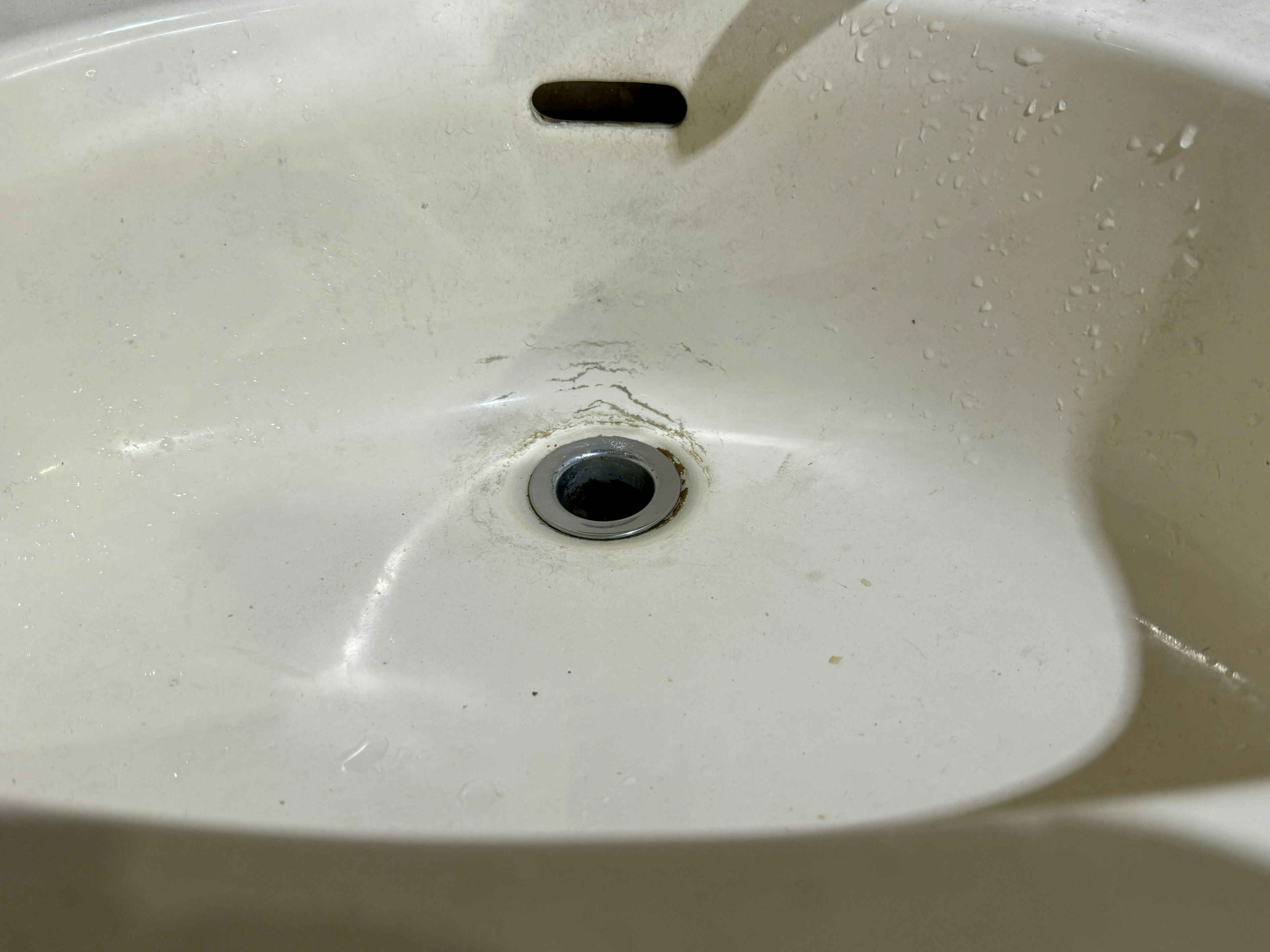 Close-up of a white sink with water droplets around the drain