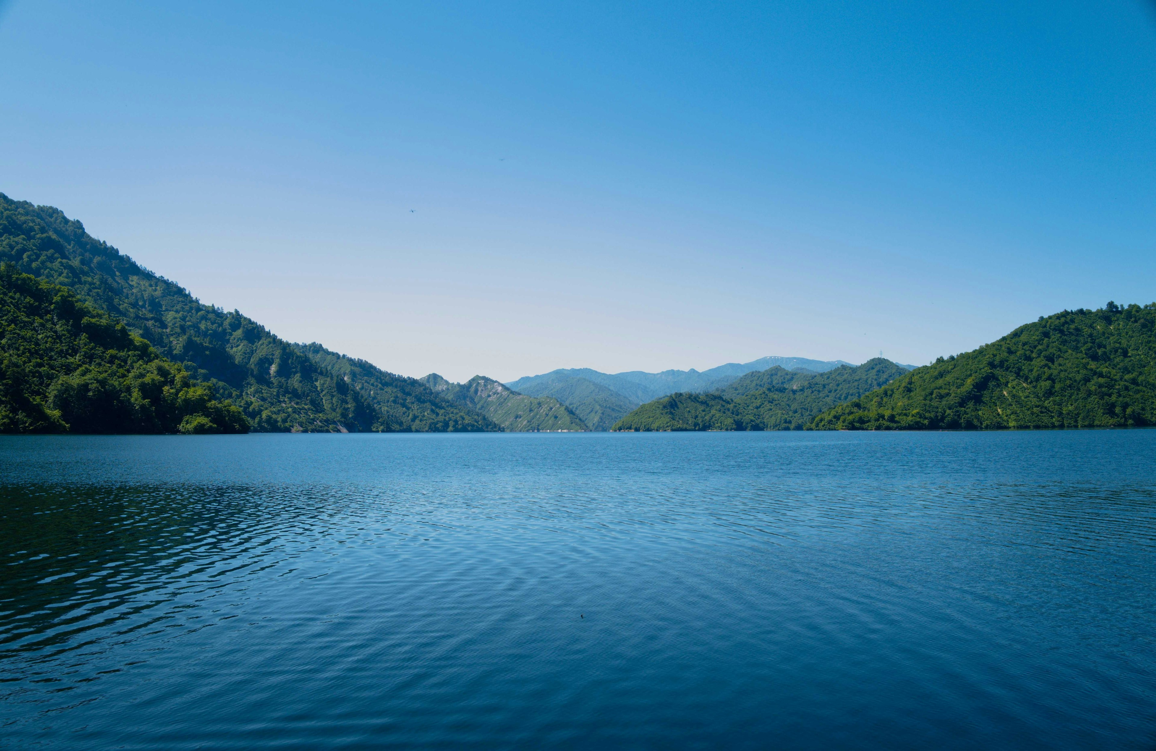 Lac serein entouré de montagnes verdoyantes sous un ciel bleu clair