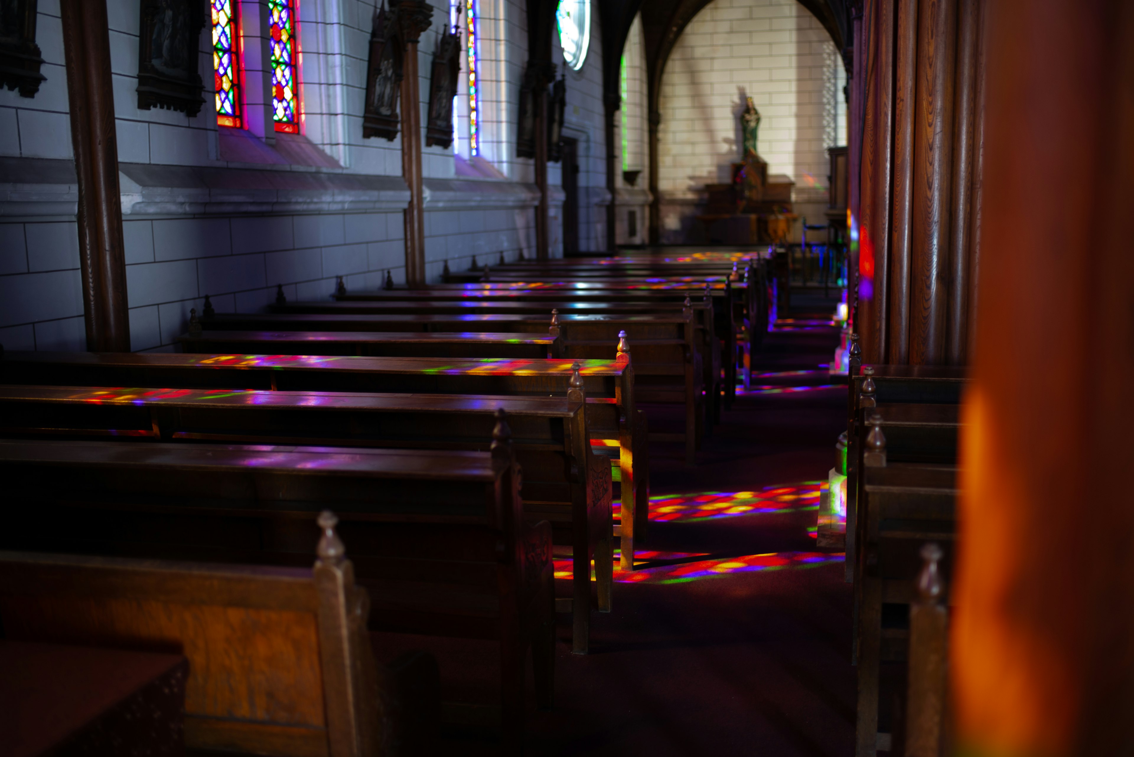 Innenraum einer Kirche mit langen Bänken und buntem Licht von Buntglasfenstern