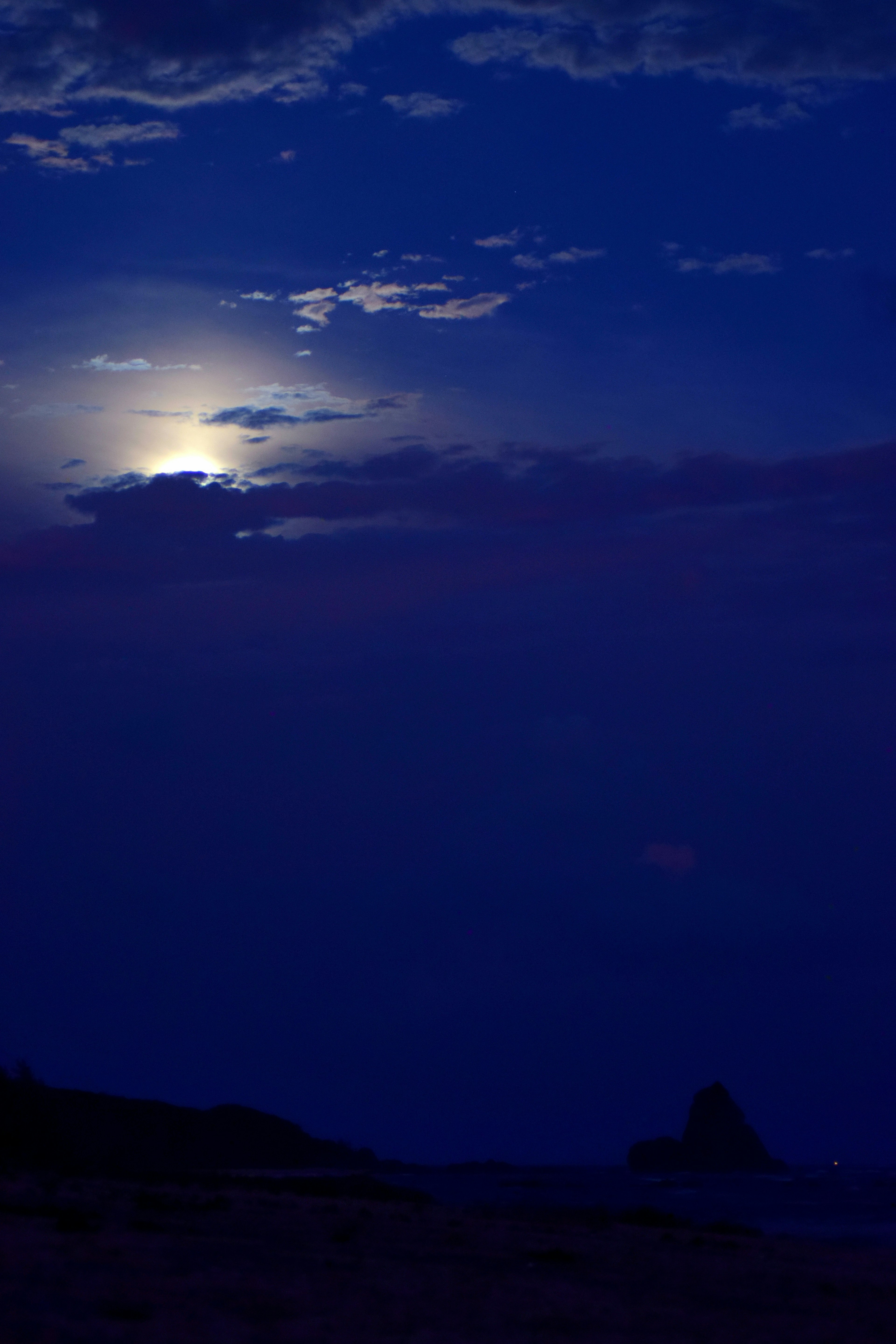 Blue night sky with a glowing moon and silhouetted clouds