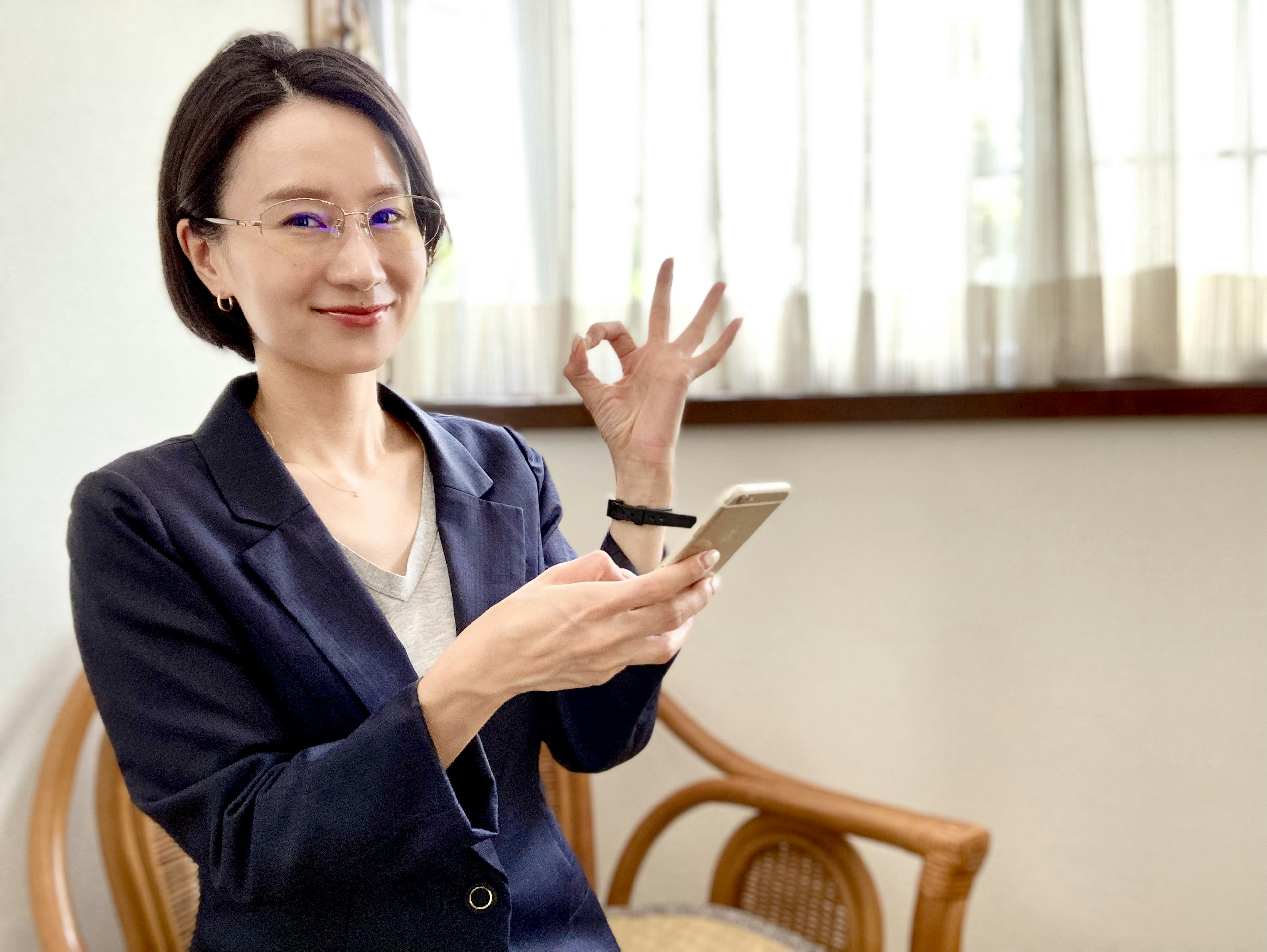 Mujer sosteniendo un teléfono inteligente haciendo un signo de OK con los dedos