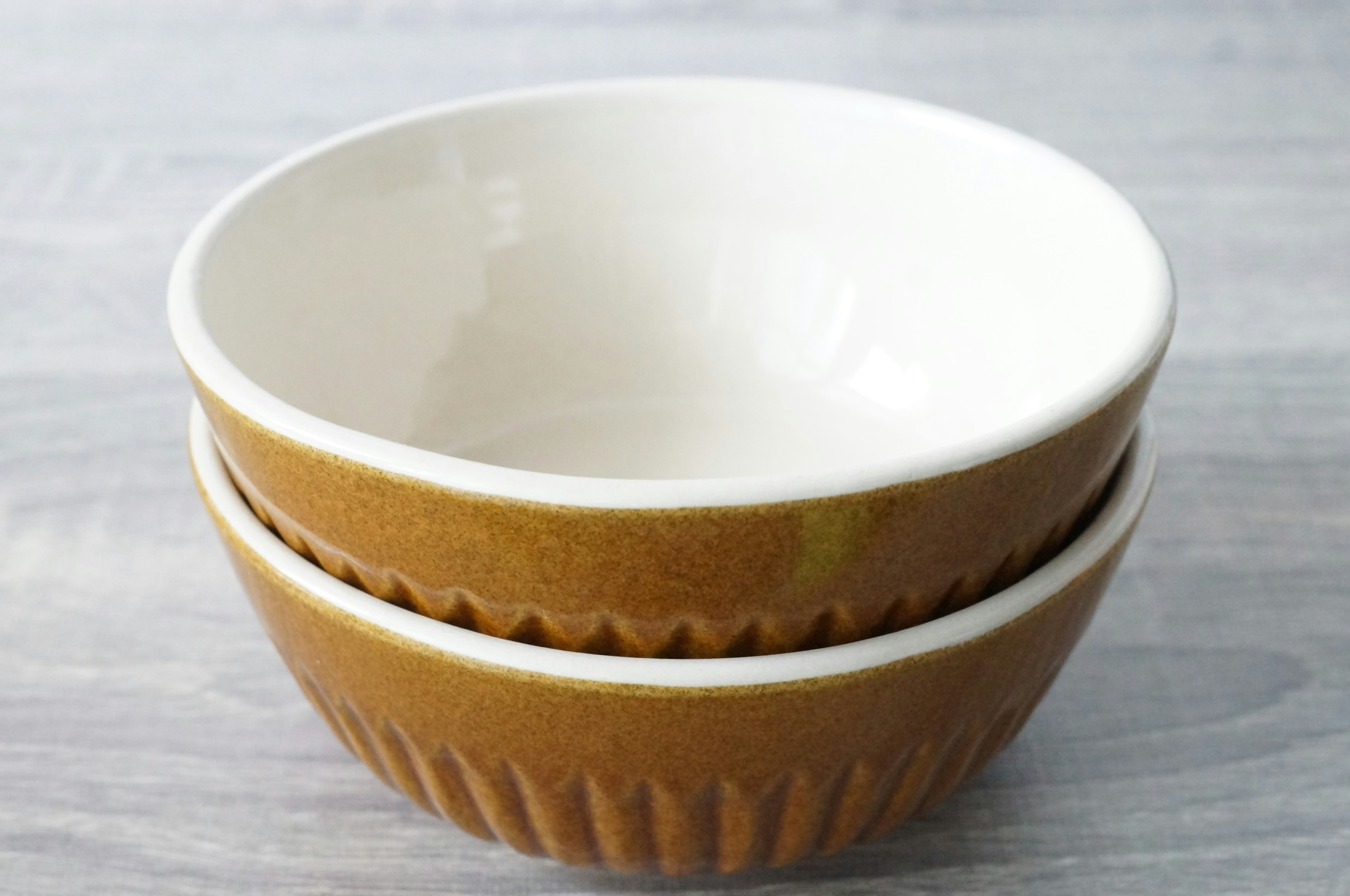 Two ceramic bowls stacked together featuring a white interior and brown exterior design