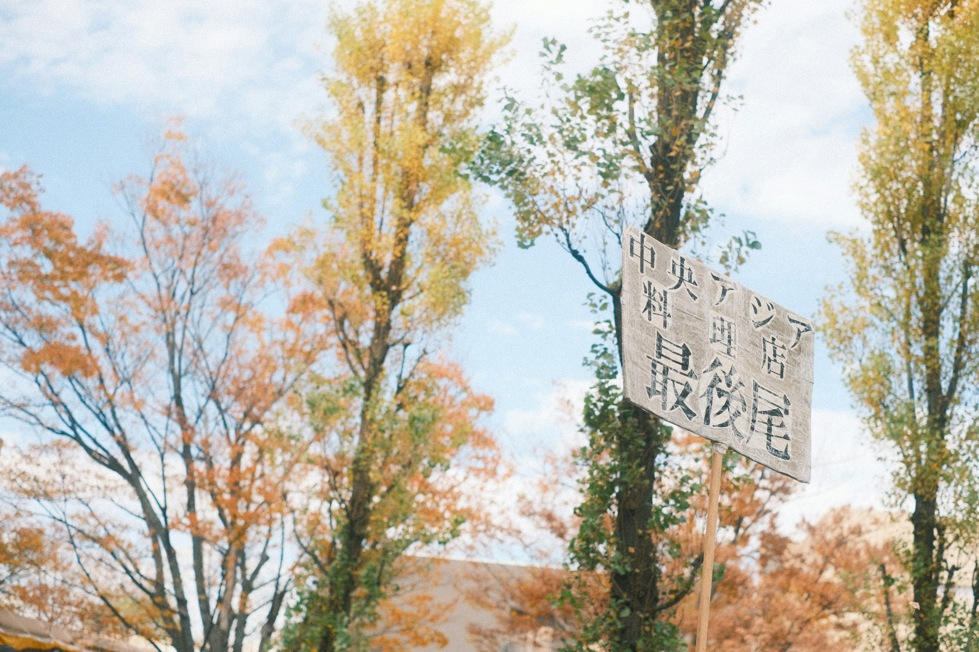 Herbstszene mit gelben Bäumen und blauem Himmel mit einem auffälligen Schild in Kanji