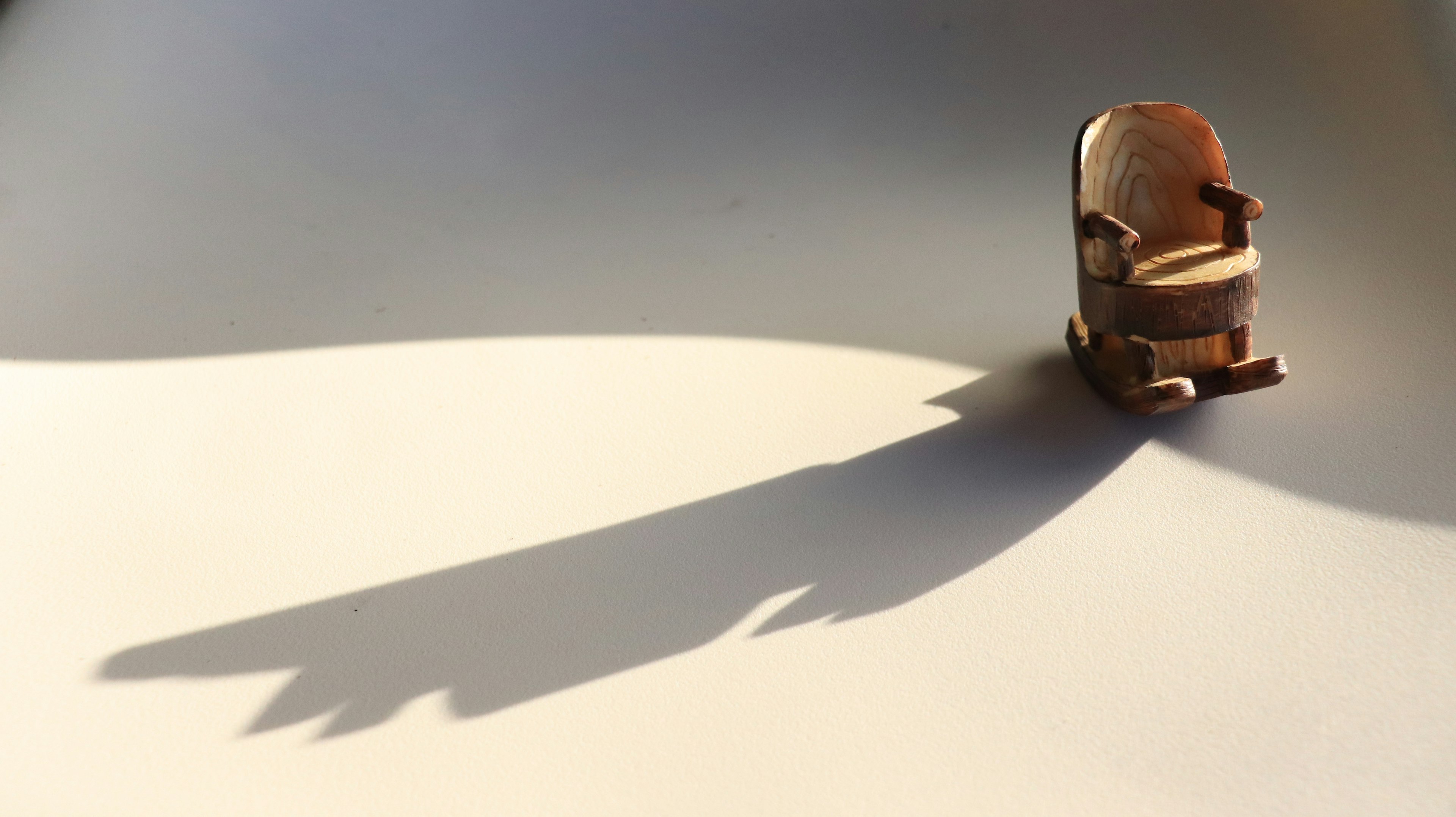 A small wooden chair on a white background casting a shadow