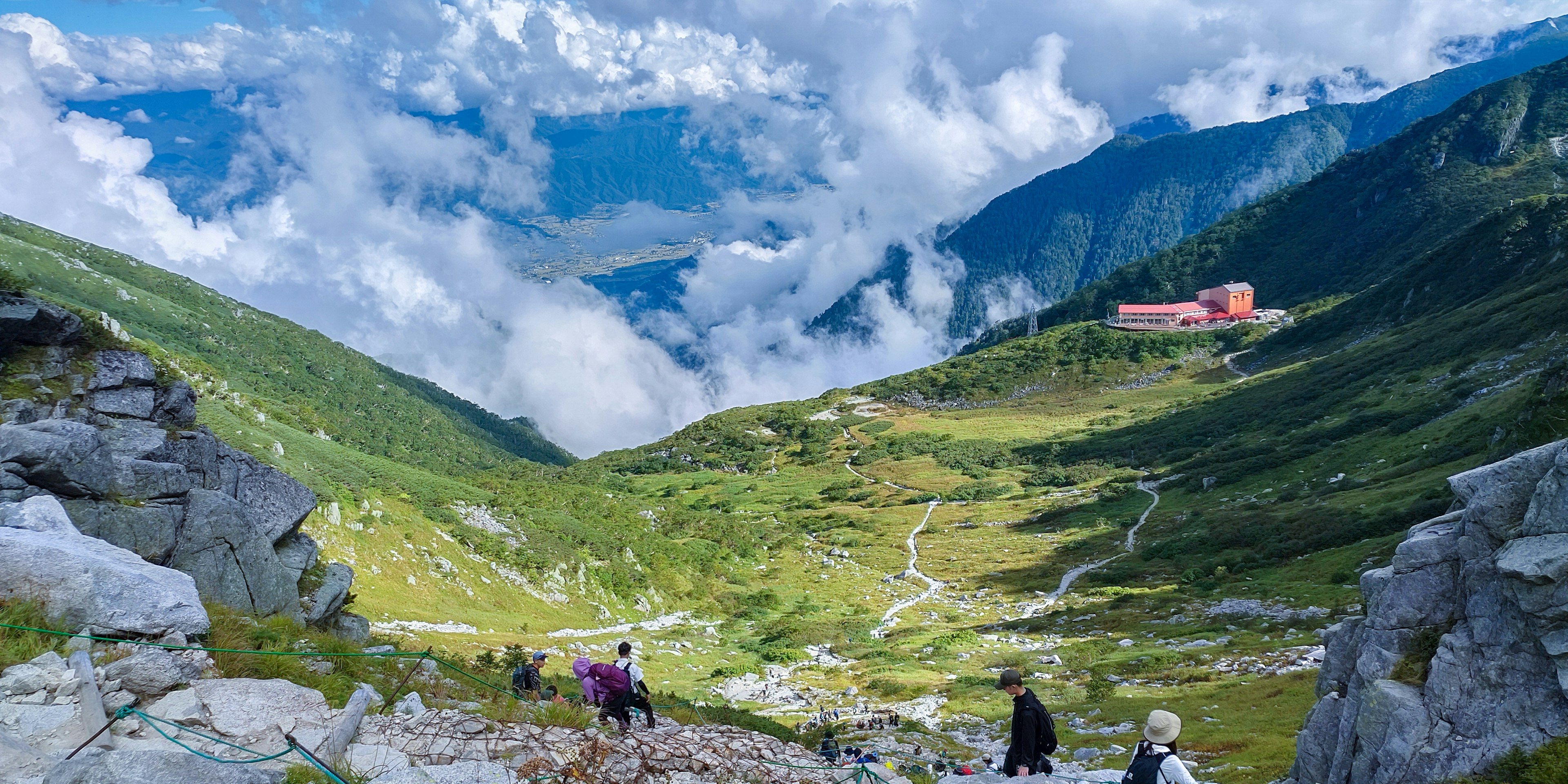 Wanderer, die einen Bergweg mit einem malerischen Tal und Wolken hinuntergehen