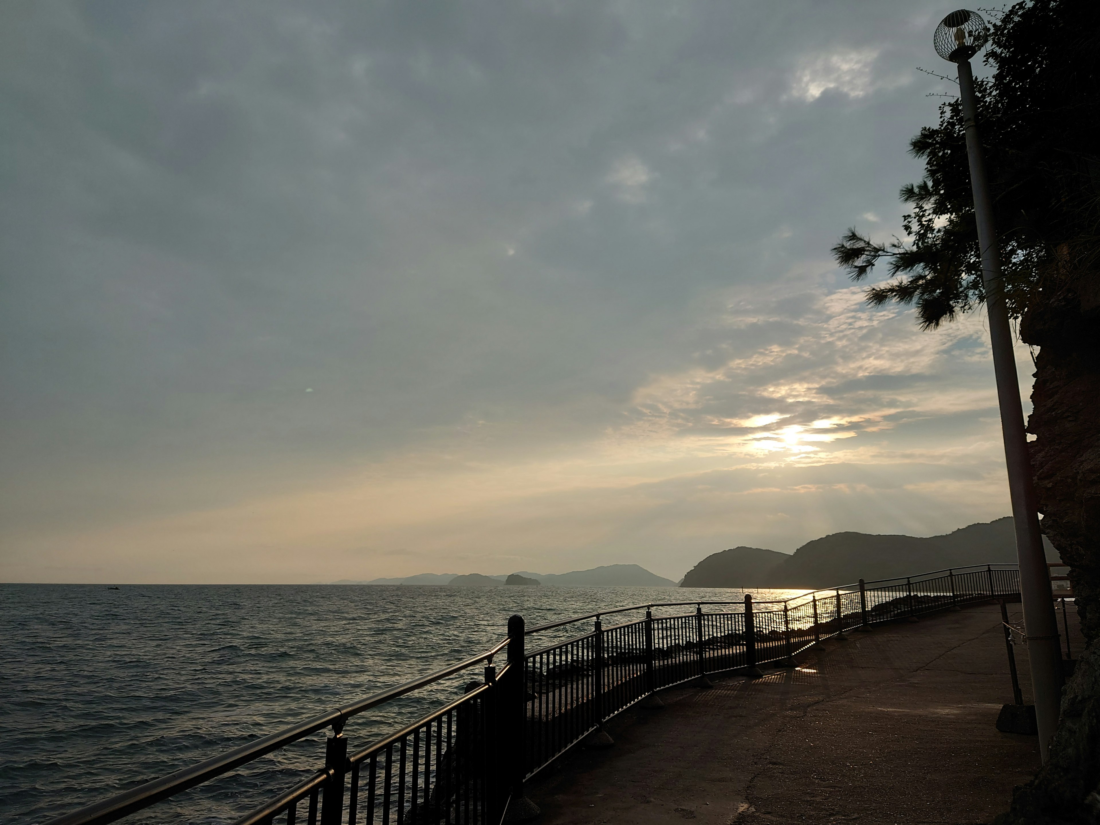 Camino costero con vista al atardecer sobre el mar y montañas