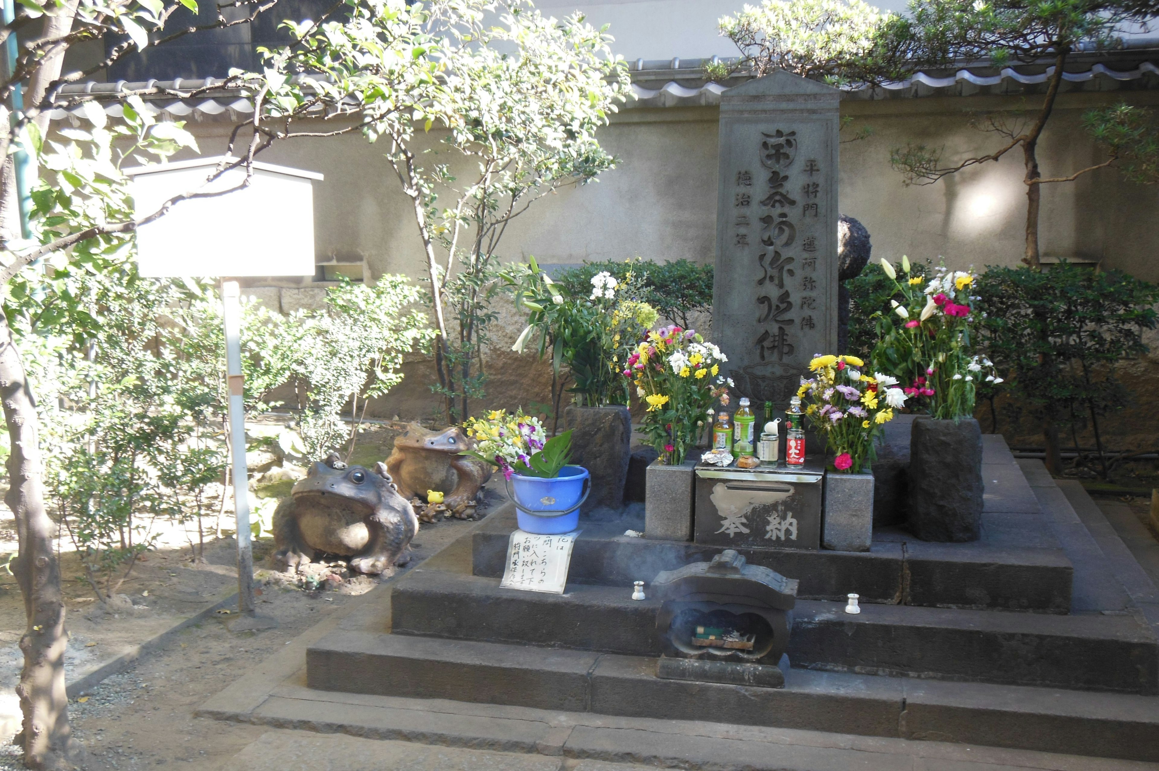 Un luogo memoriale sereno con un monumento di pietra circondato da fiori e offerte