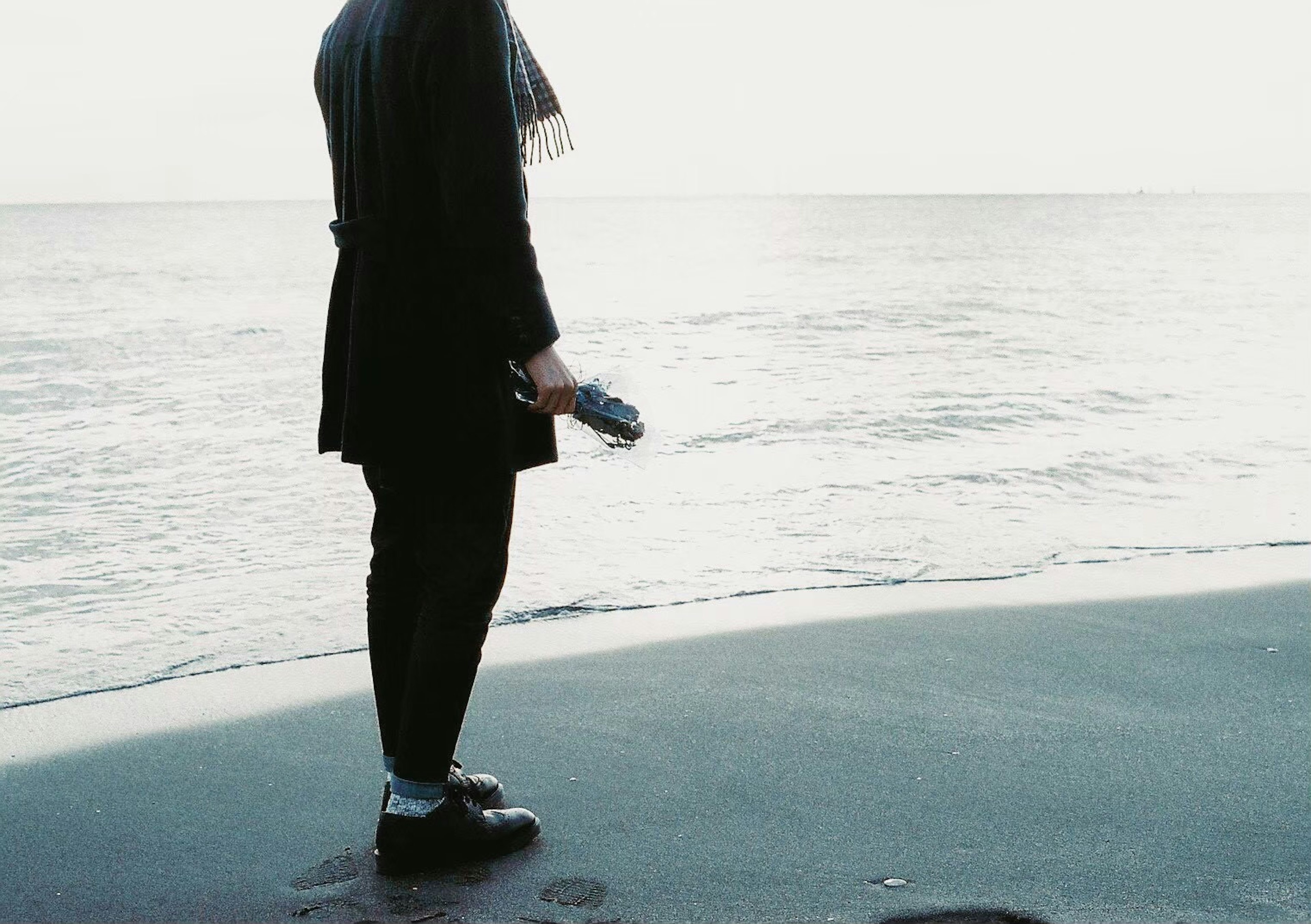 A figure standing by the seaside holding something in their hand