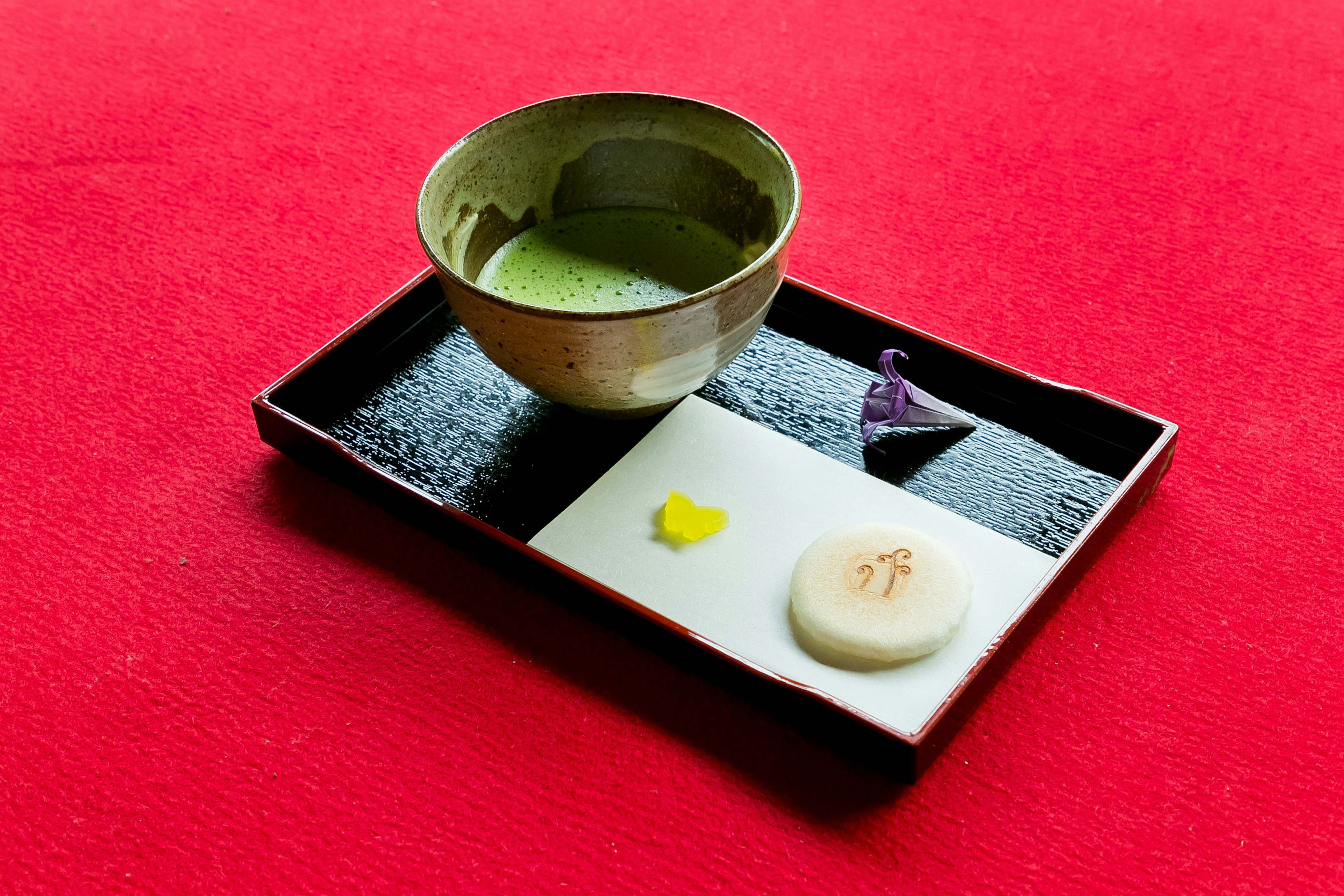 Una bandeja negra con té matcha y dulces japoneses sobre un fondo rojo