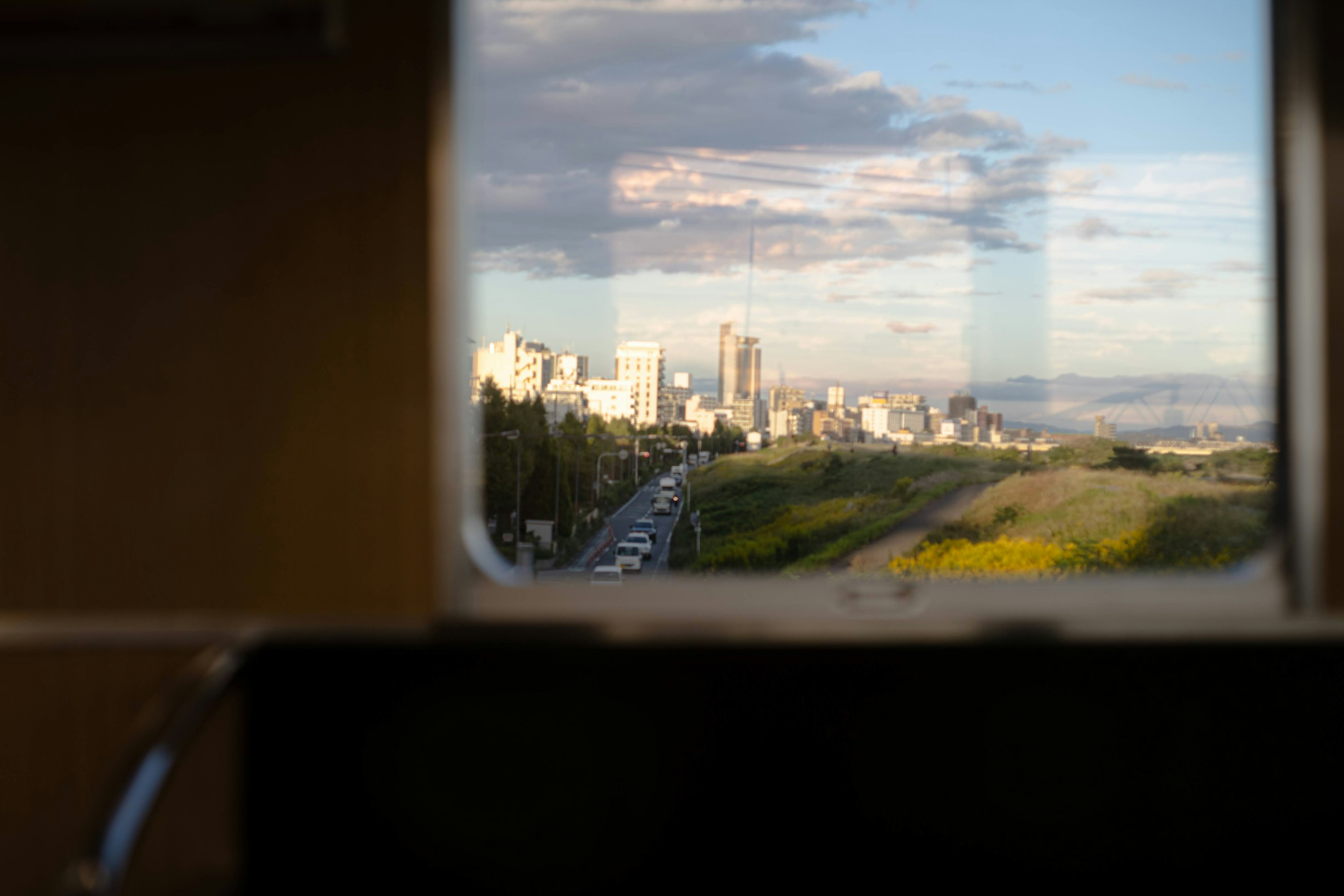 Stadtansicht durch ein Fenster, blauer Himmel mit Wolken, Grünflächen und Verkehr