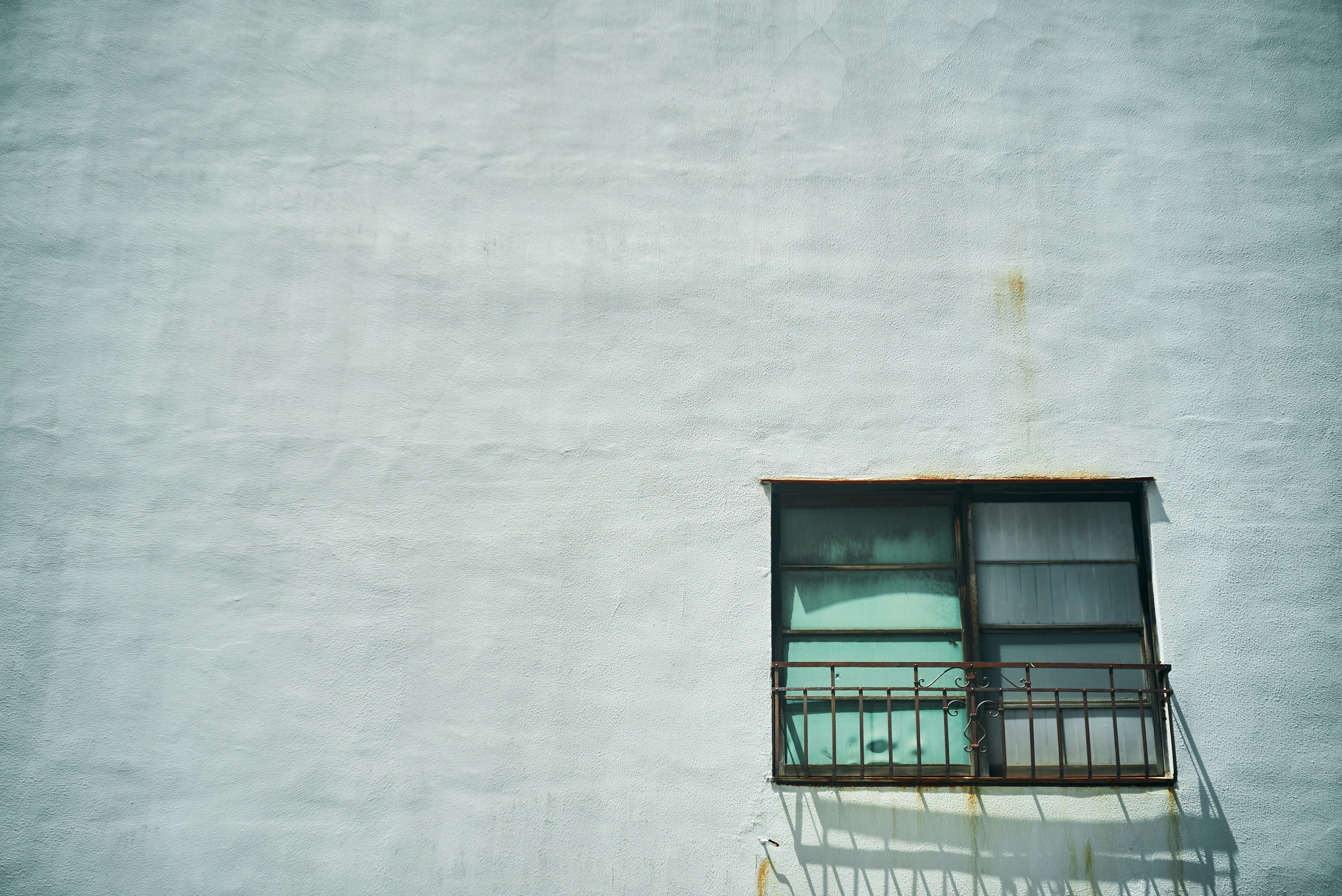 Façade simple d'un bâtiment avec une fenêtre noire et un balcon sur un mur blanc