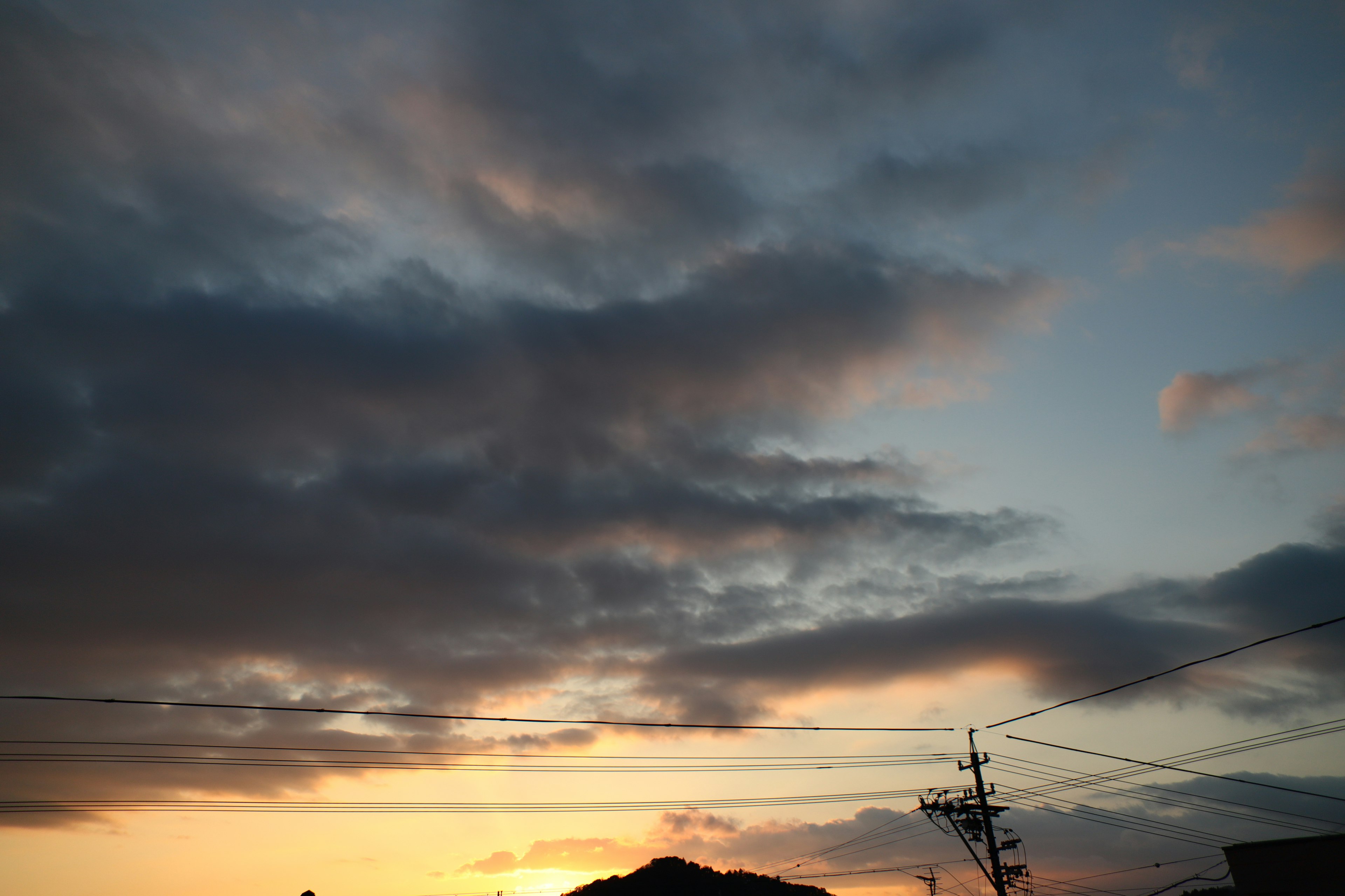 Cielo al tramonto con nuvole e silhouette di pali elettrici