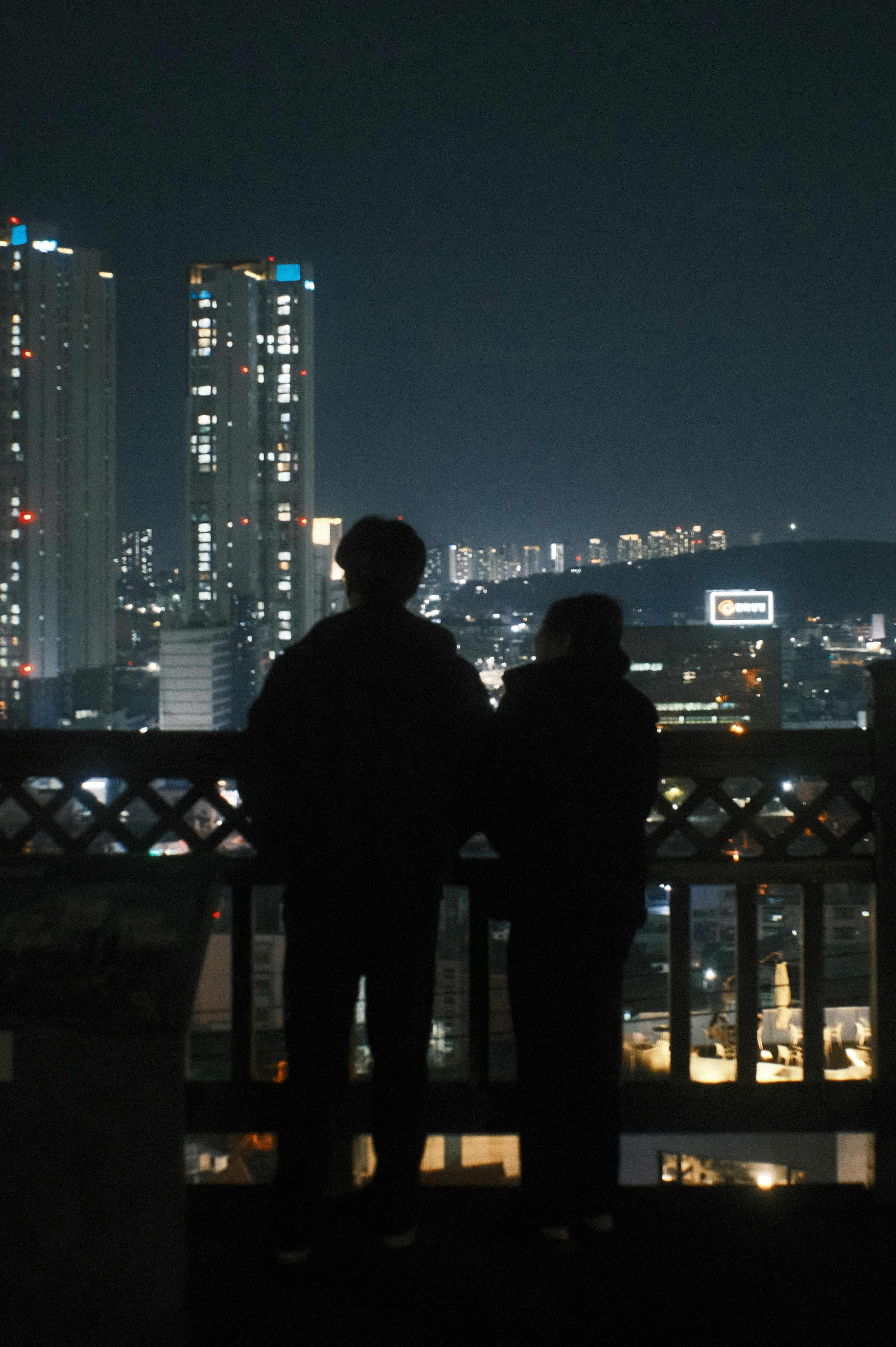 Silueta de dos personas mirando un paisaje urbano nocturno iluminado por las luces de los edificios