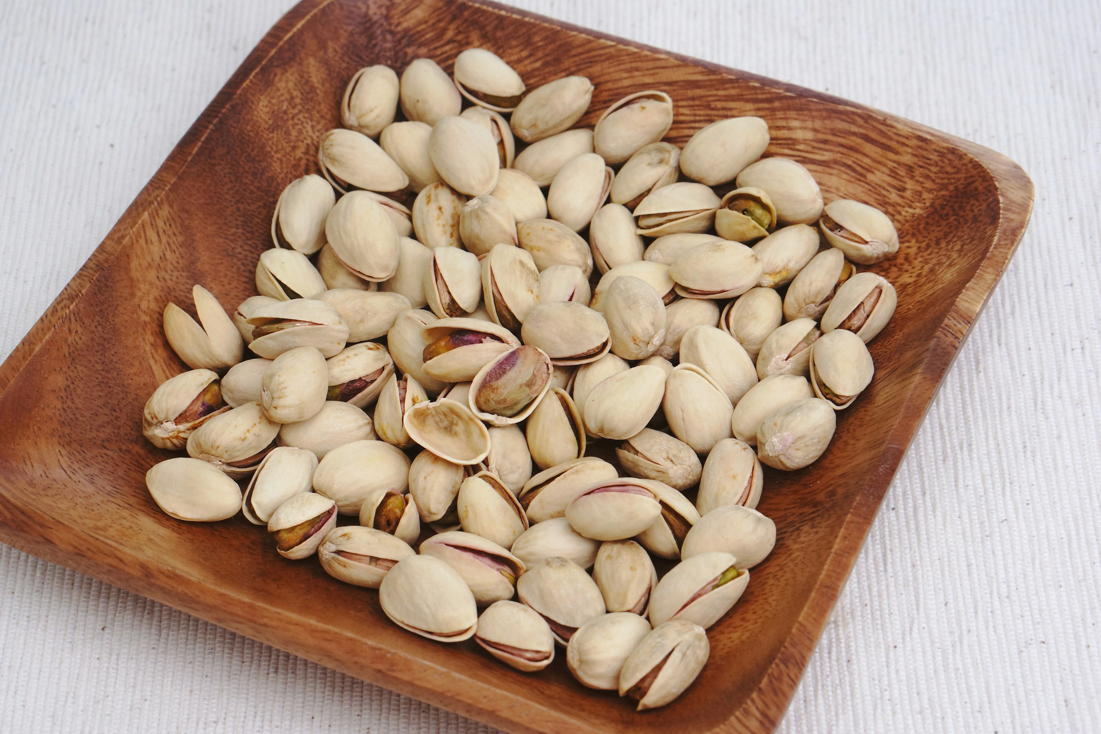 A wooden bowl filled with many pistachio shells