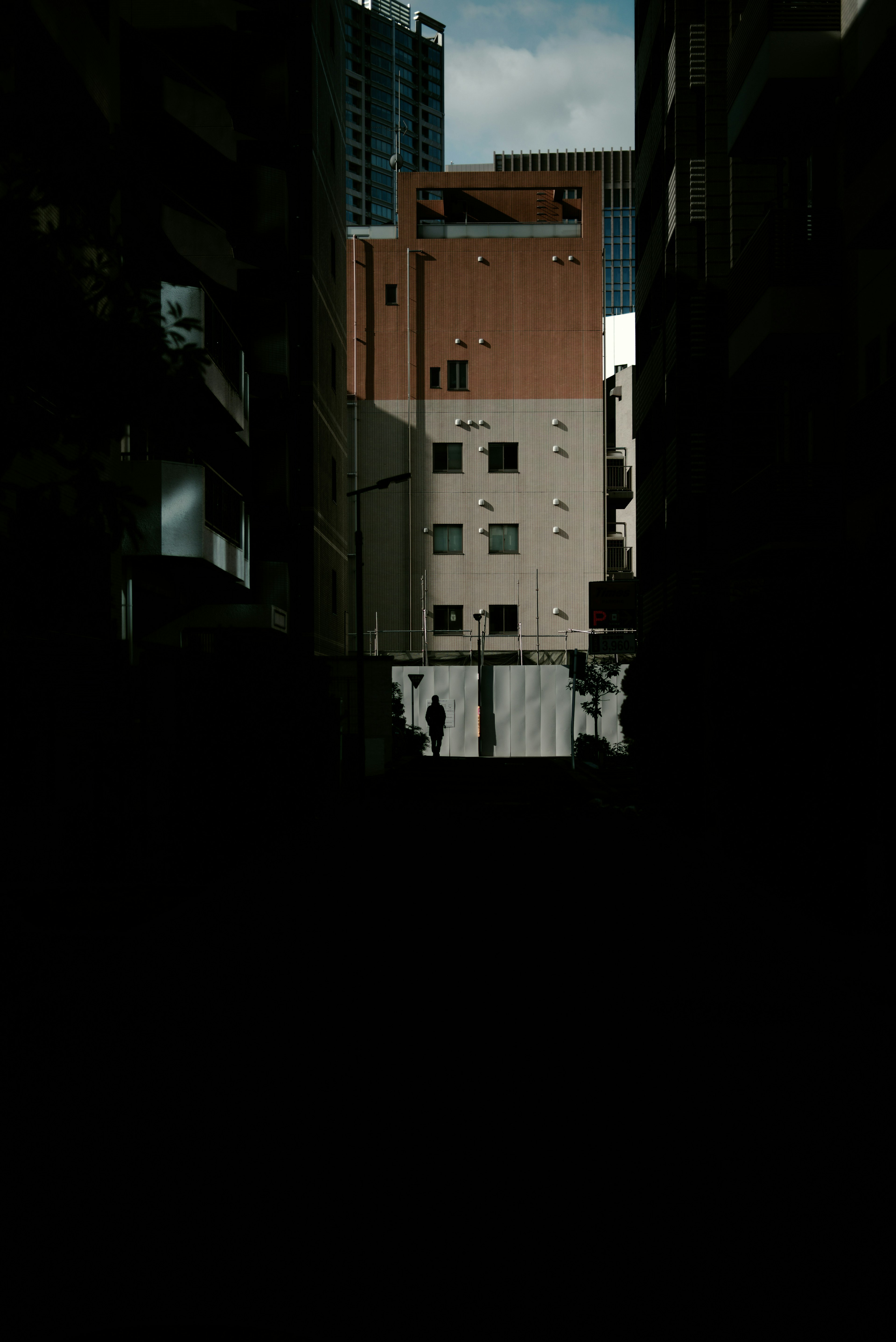 Ruelle sombre révélant des bâtiments et un ciel nuageux