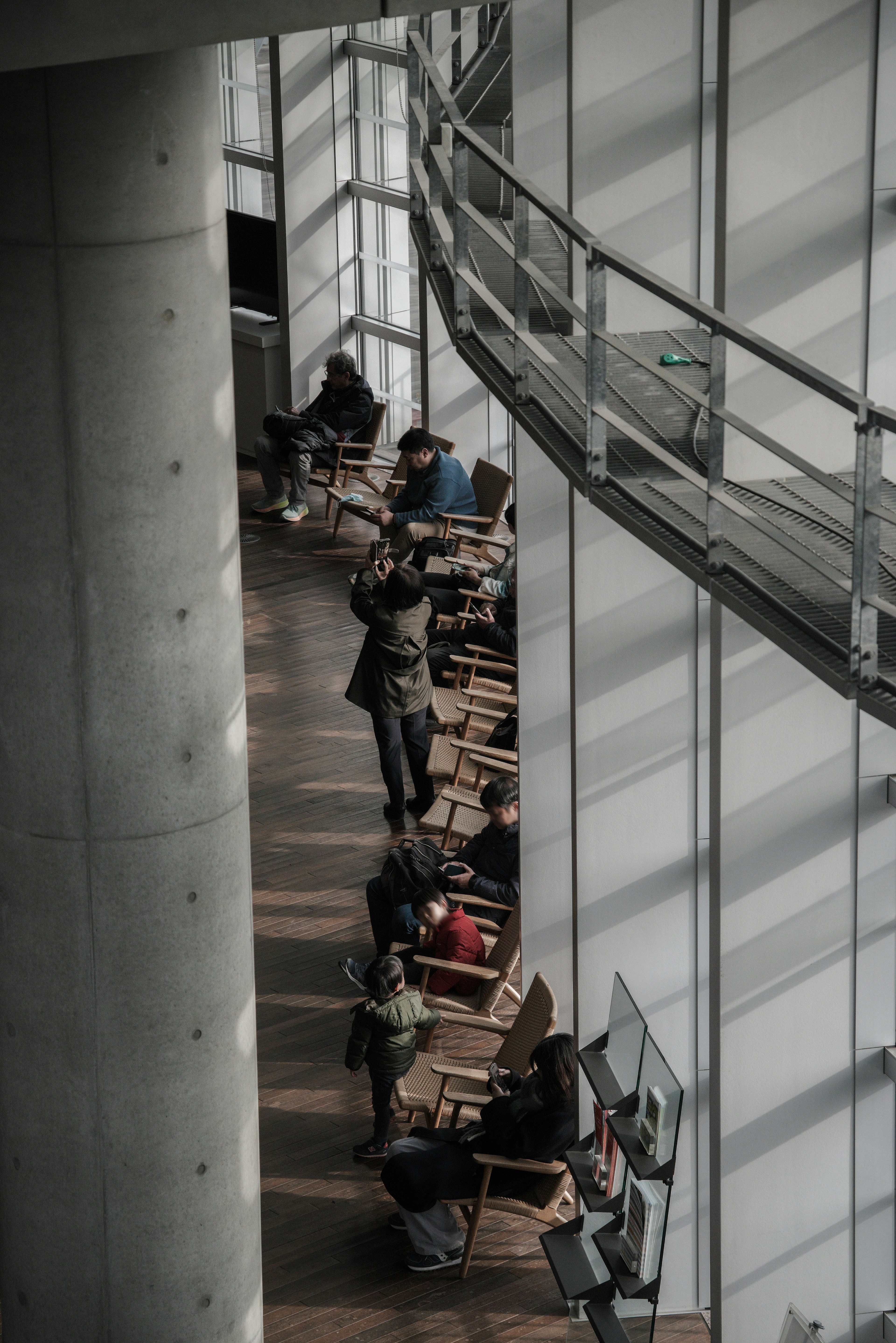 People inside a modern building sitting on chairs large windows allowing natural light