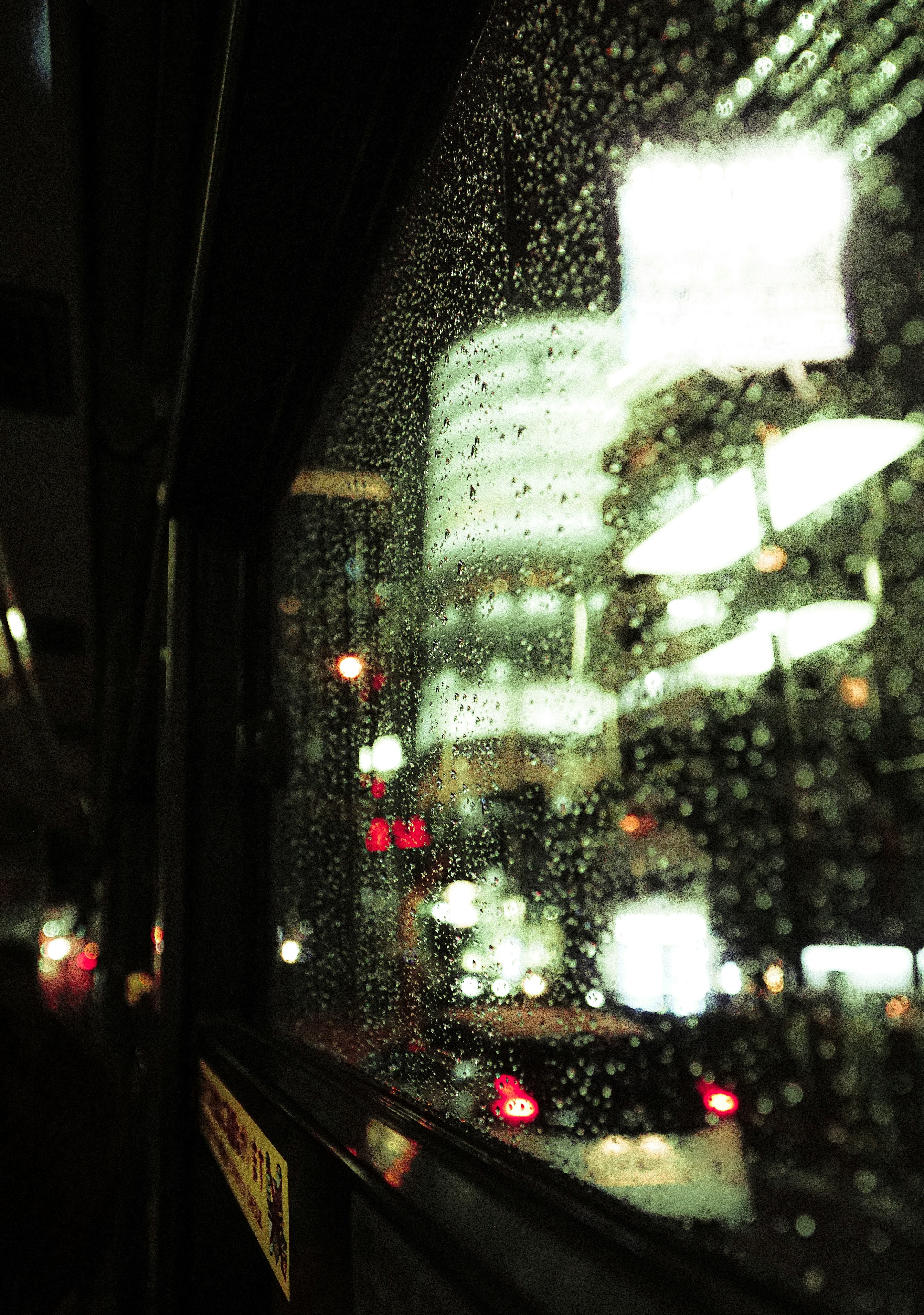 Night city lights seen through a rain-speckled bus window