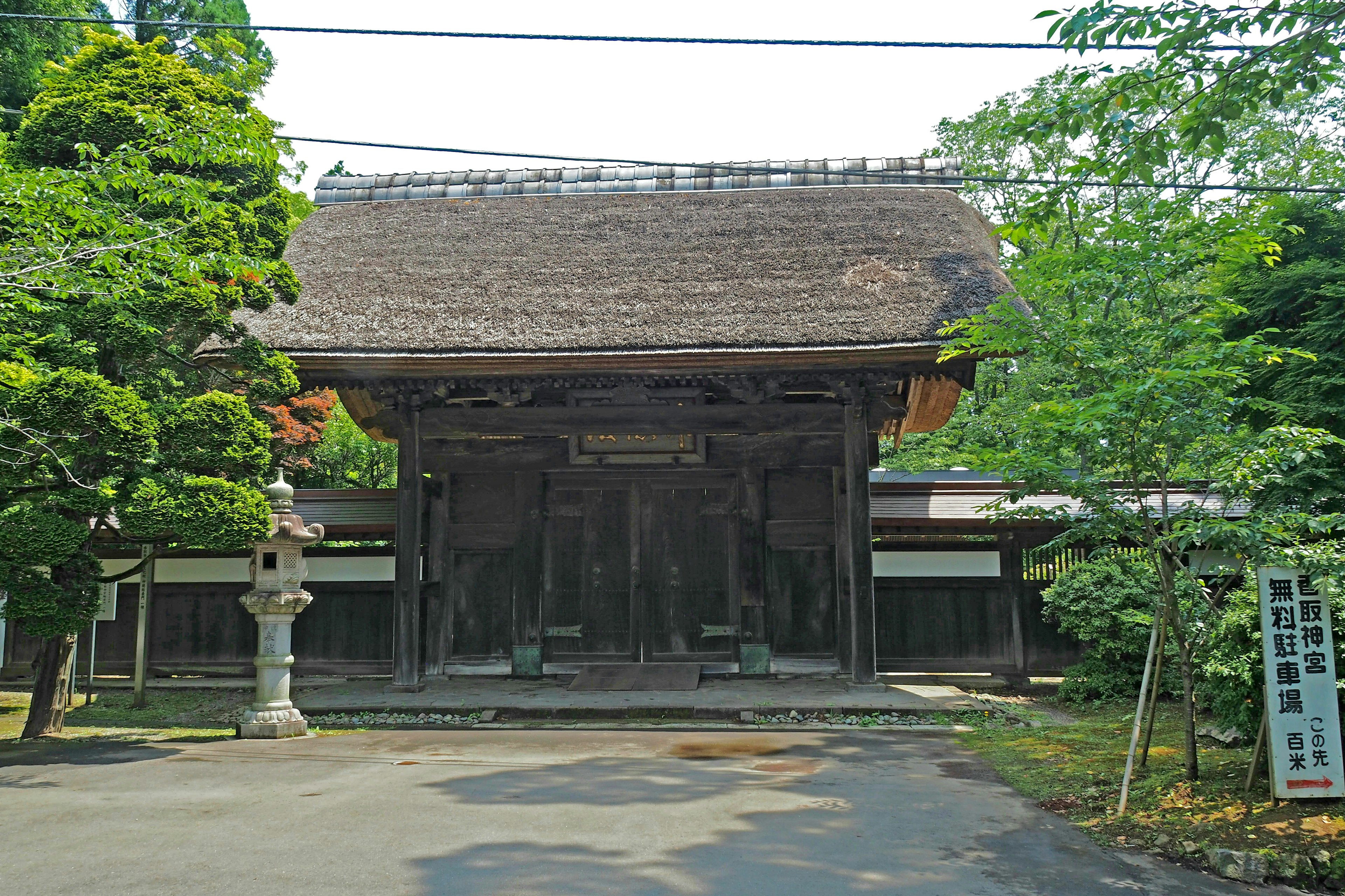 Old Japanese temple gate with thatched roof surrounded by green trees