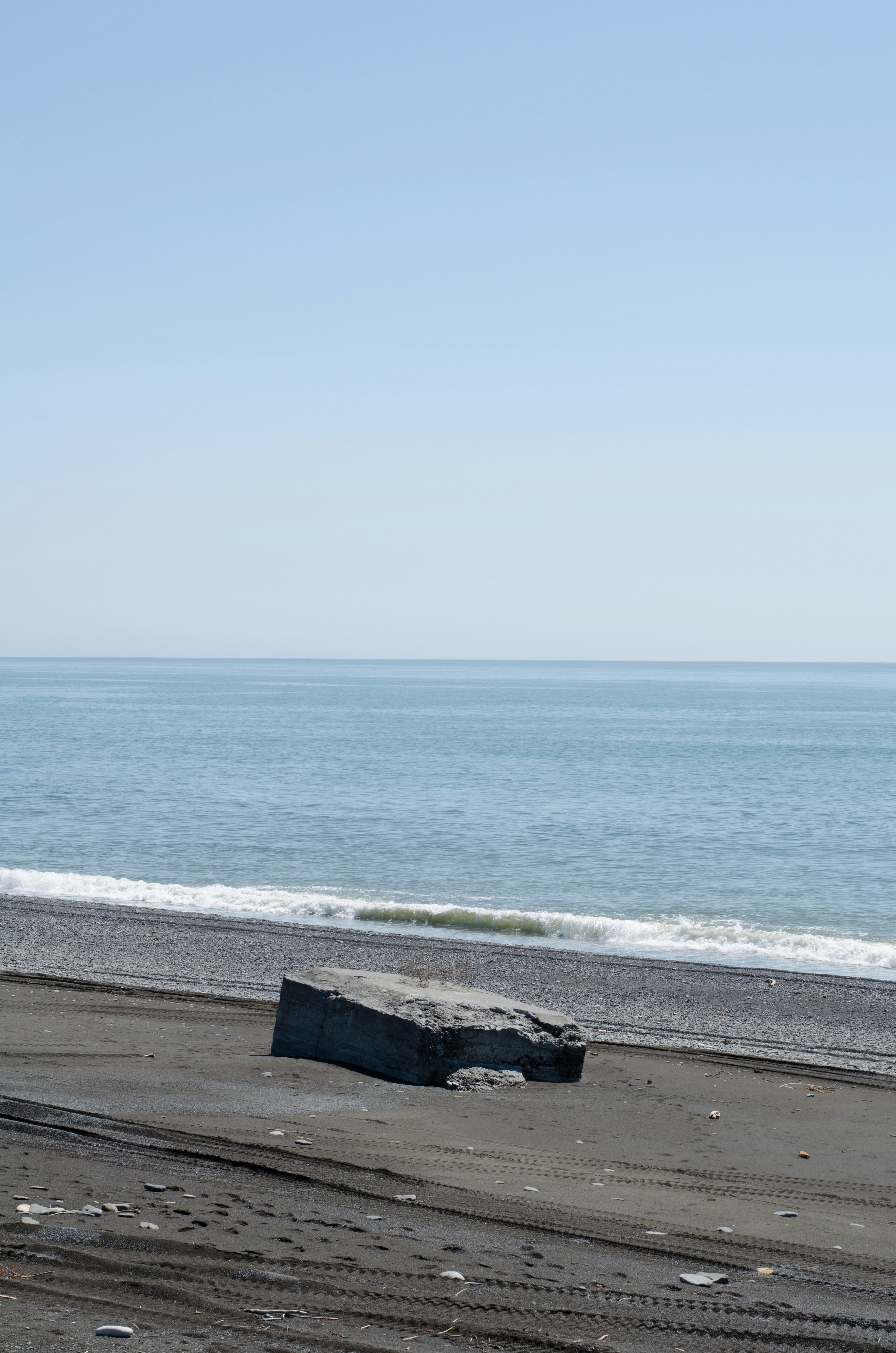 Ein schwarzes, steinähnliches Objekt an einem Sandstrand unter einem ruhigen Meer und blauem Himmel