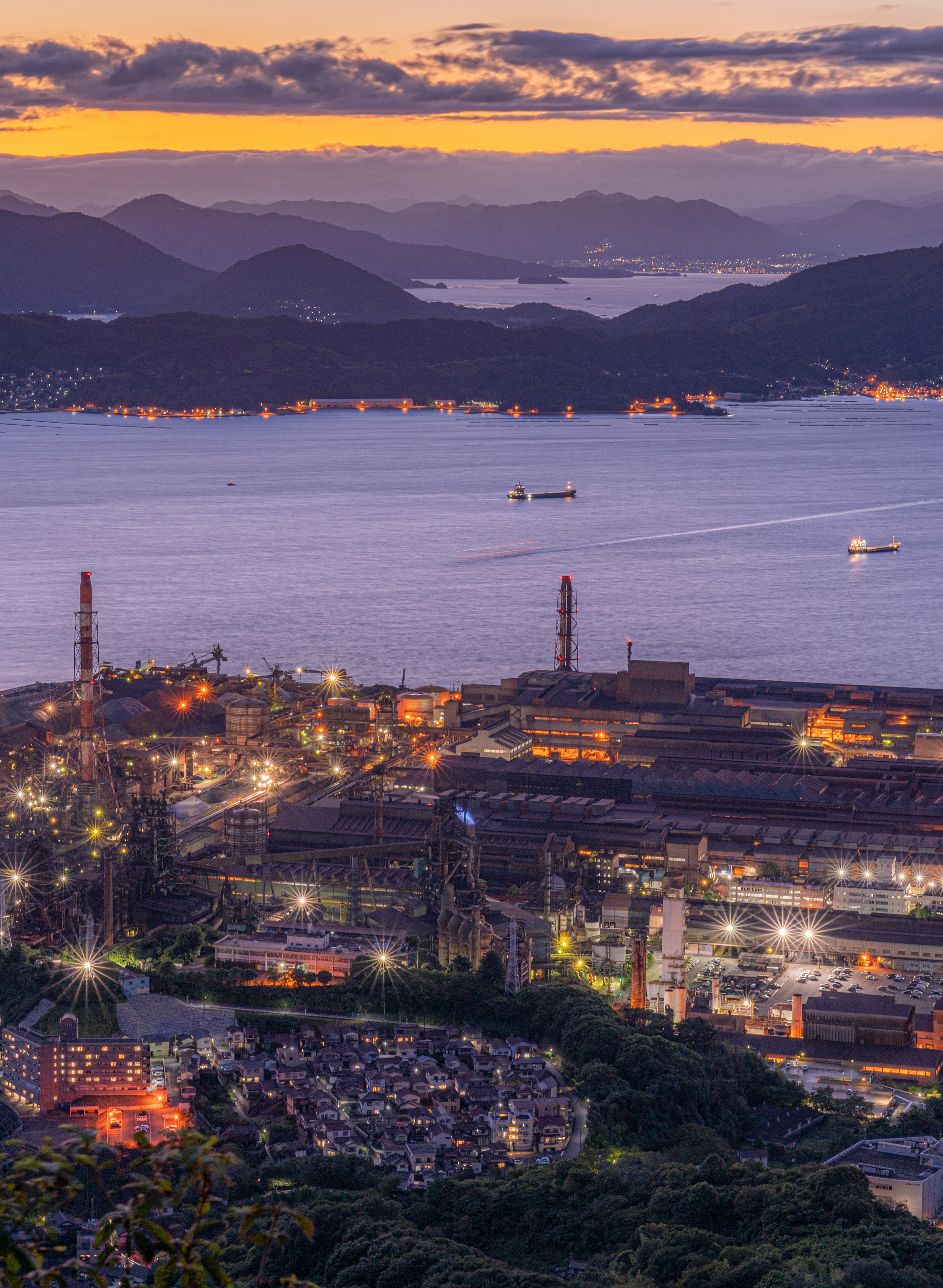 Panoramic view of an industrial area at sunset with water and mountains