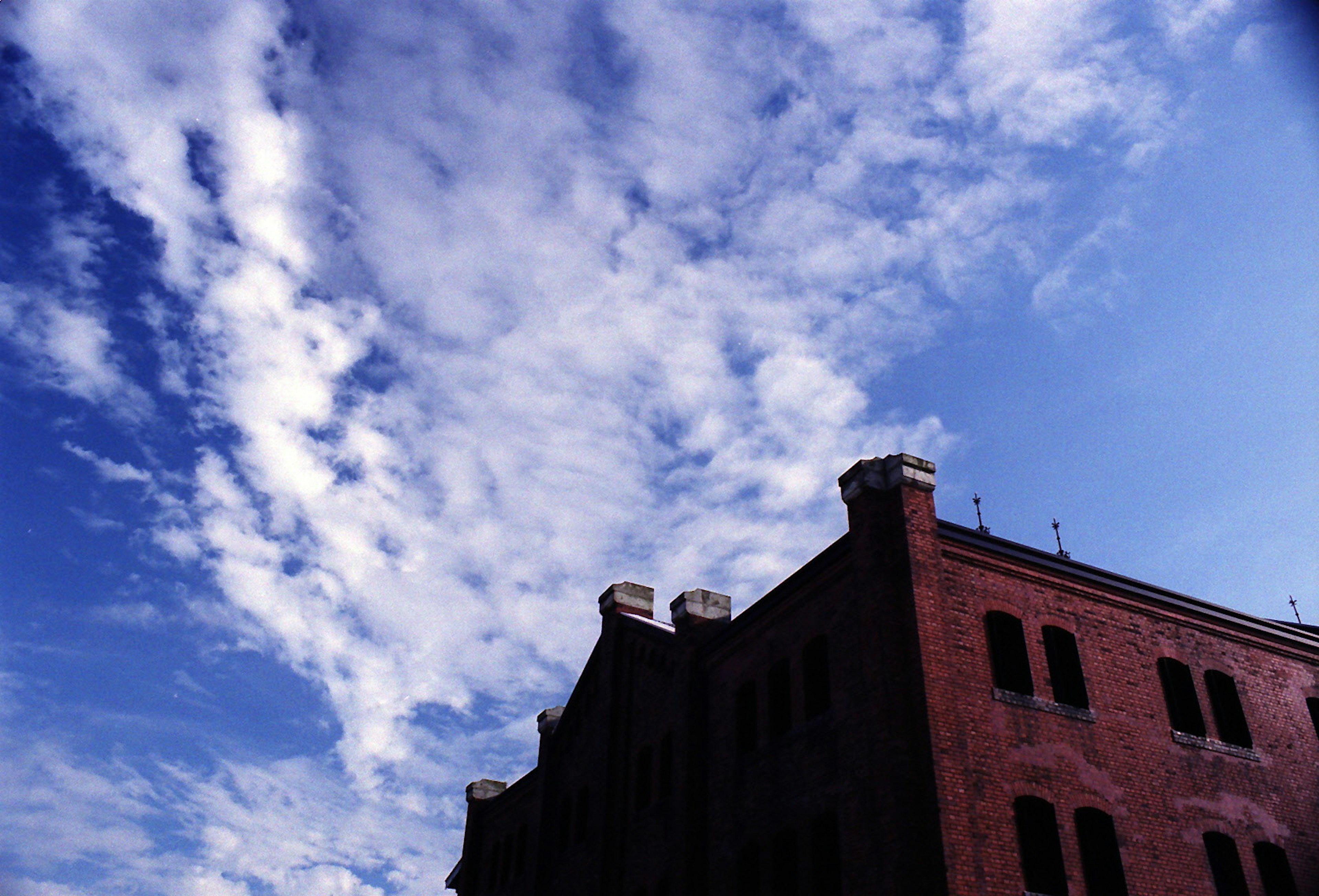 Silhouette of a red building against a blue sky with white clouds