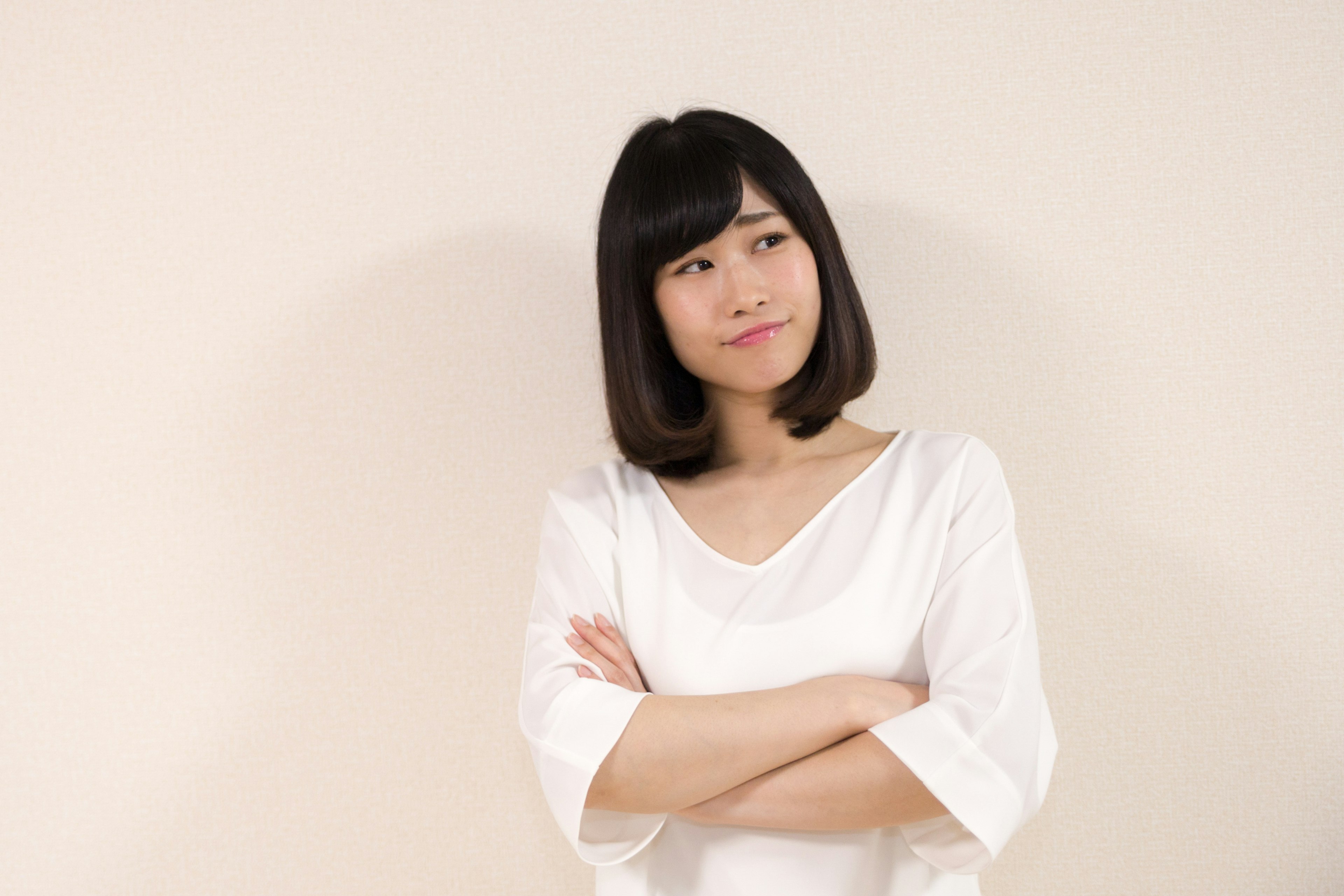 A woman in a white top appears thoughtful with crossed arms